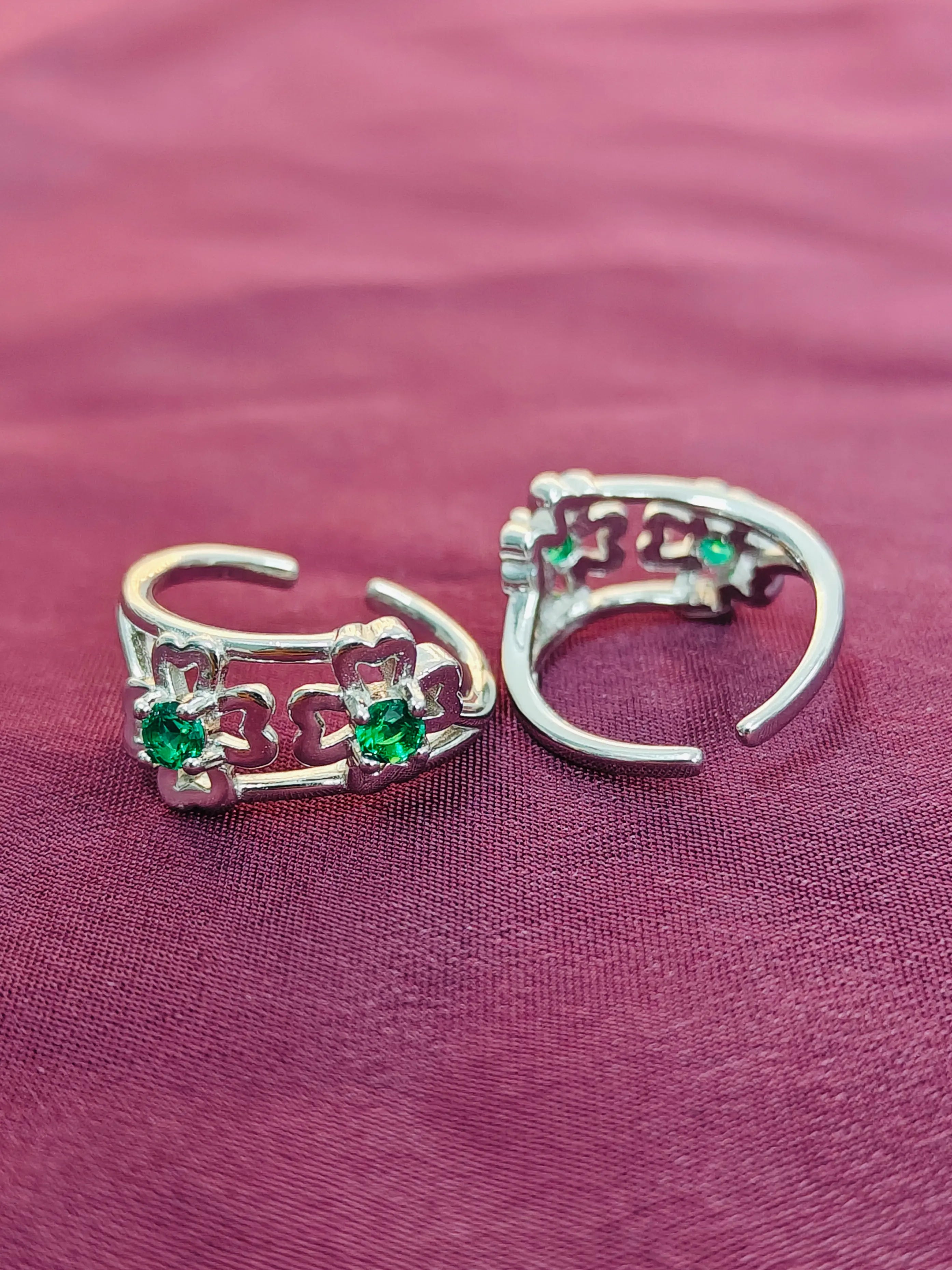 Silver hoop earrings with green gemstones on a purple fabric background