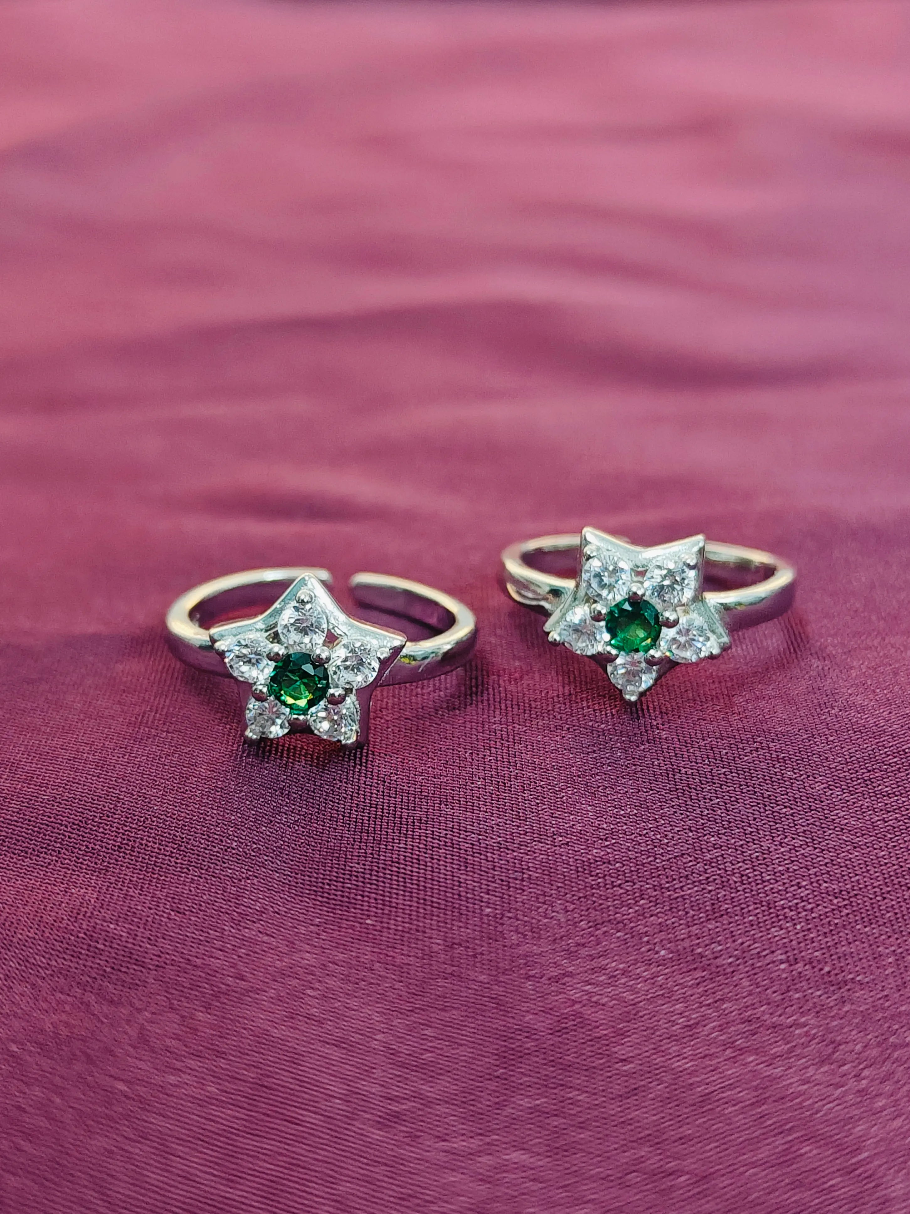 Star-shaped silver rings with green gemstones on a purple fabric background