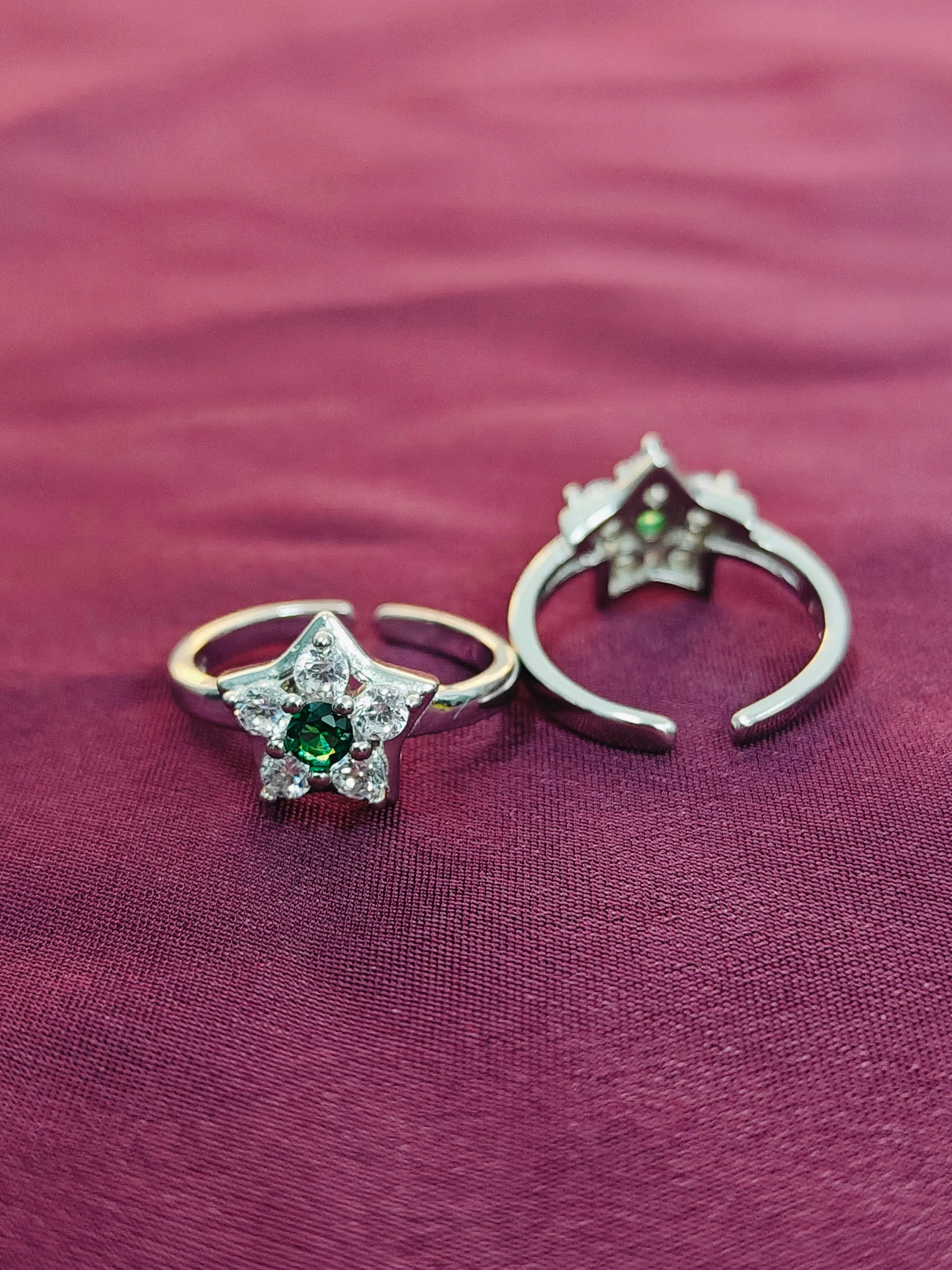 Two rings with star-shaped designs and green gemstones on a purple fabric background