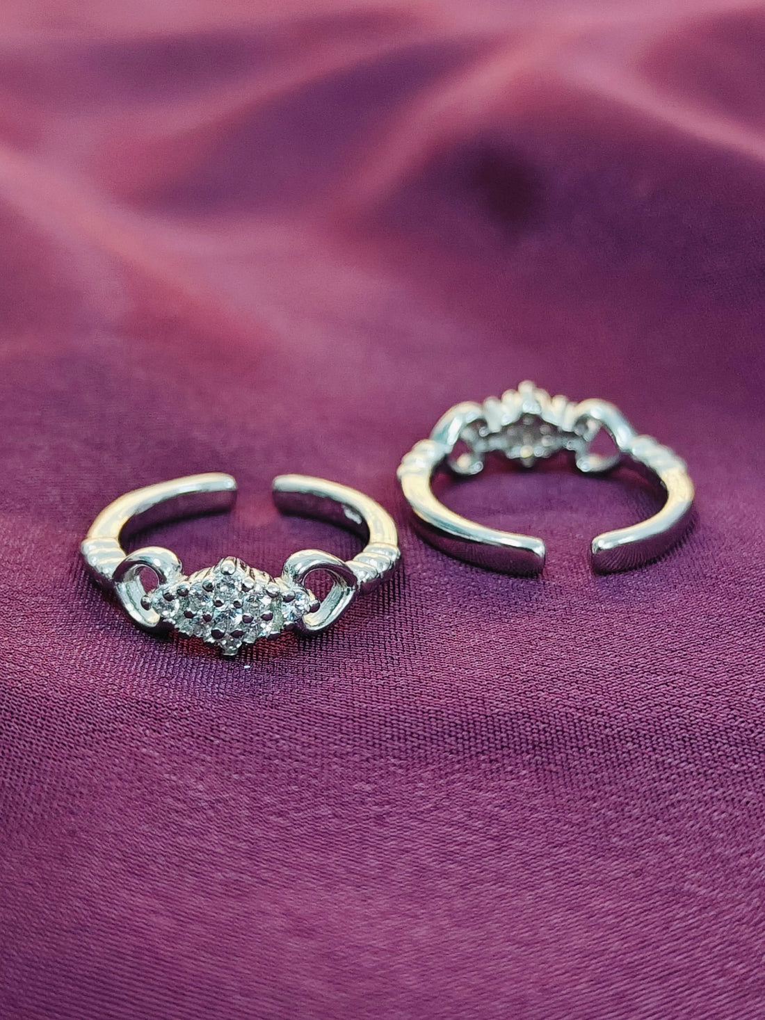 Pair of silver hoop earrings with heart designs on a purple fabric background