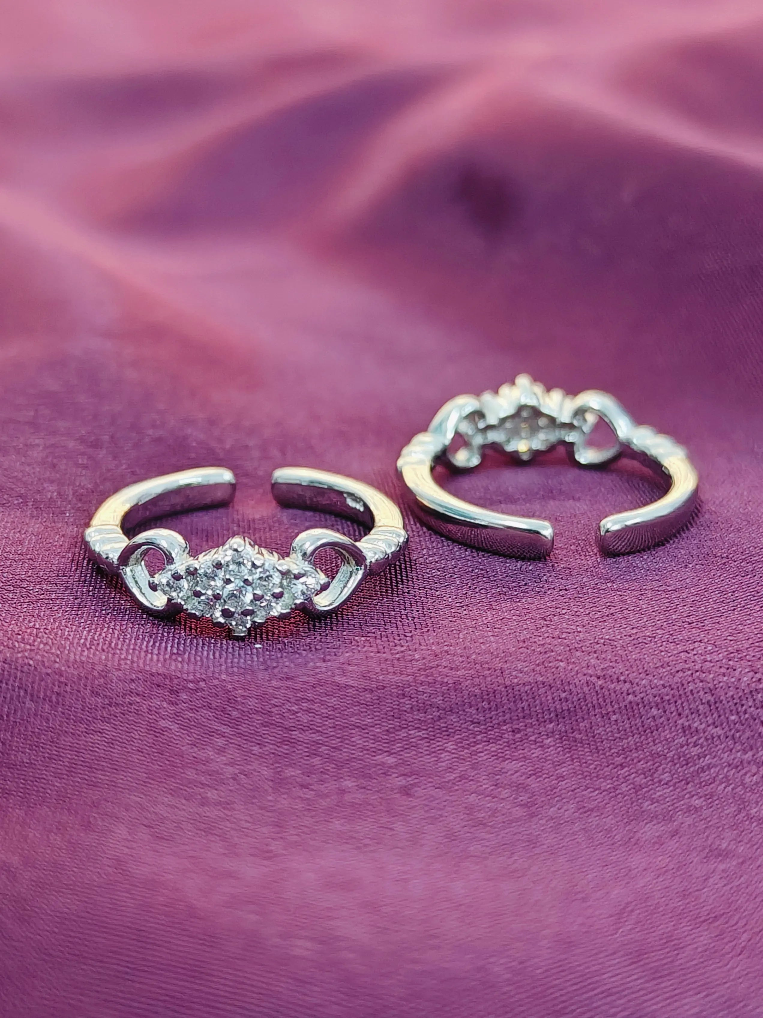 Two silver hoop earrings with heart-shaped gemstones on a purple fabric background