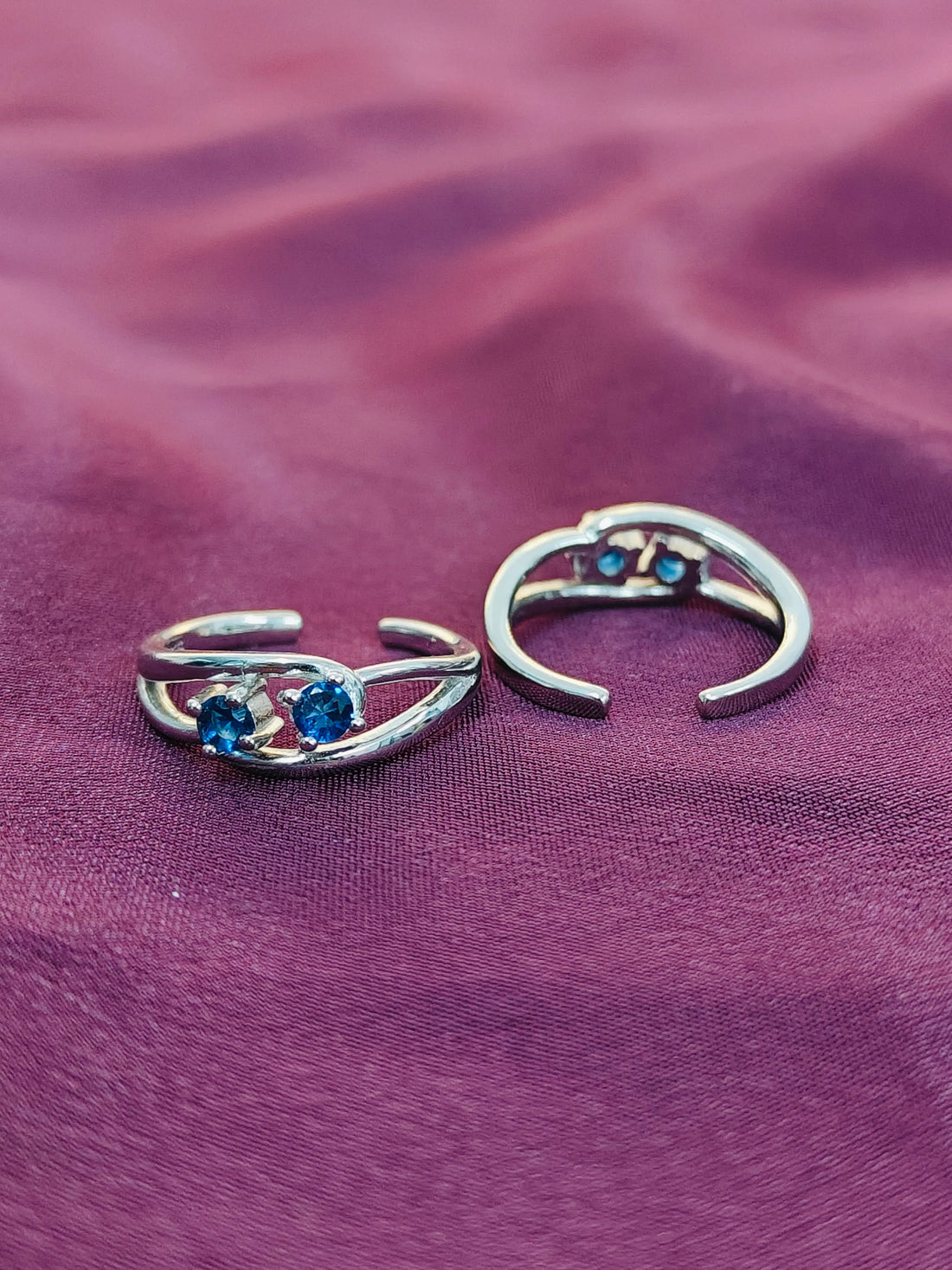 Pair of silver hoop earrings with blue gemstones on a purple fabric background