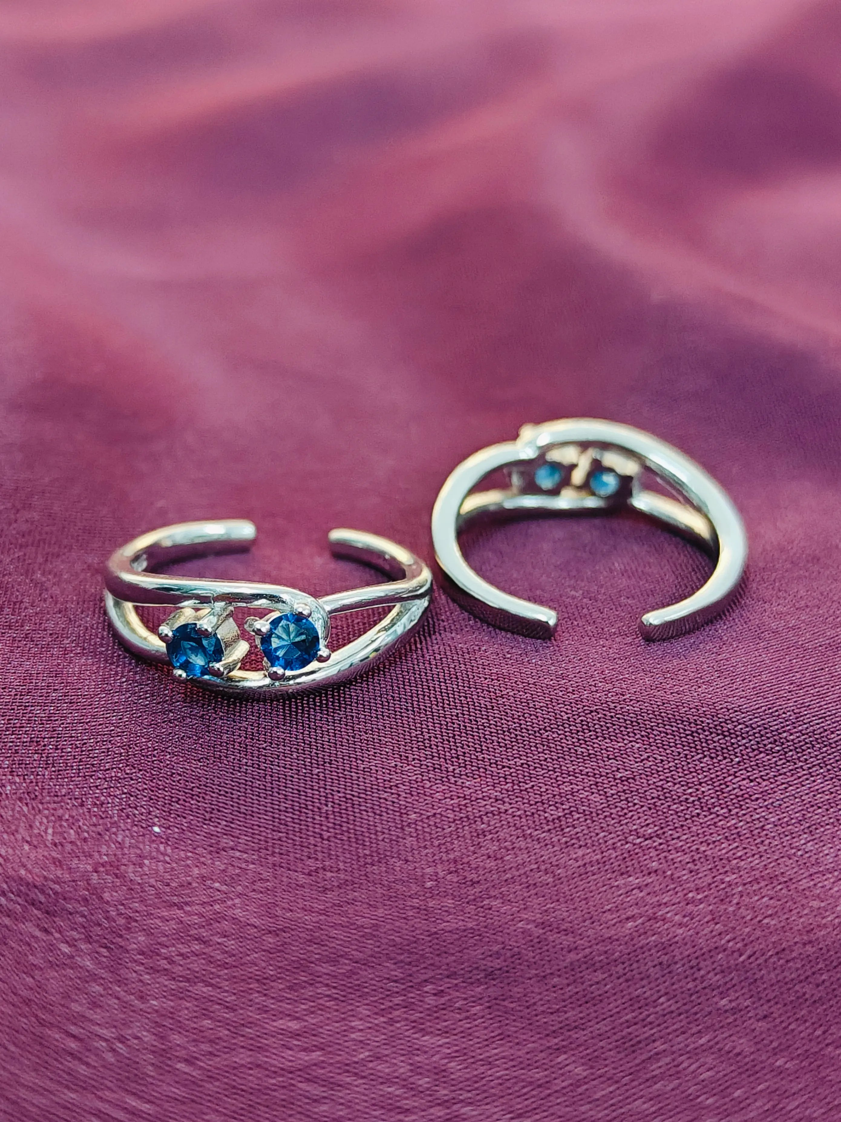 Two silver rings with blue gemstones on a purple fabric background