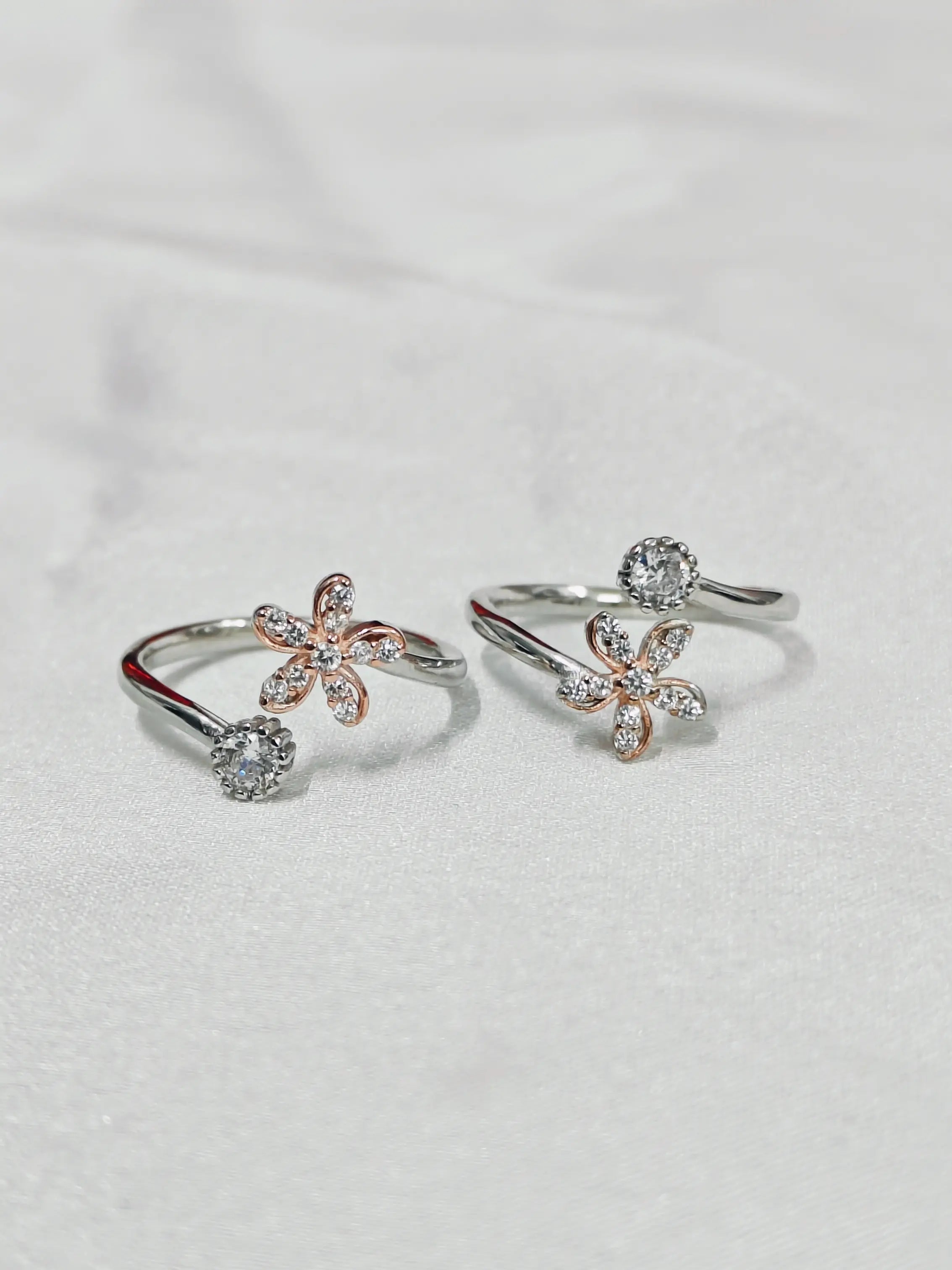 Pair of floral open rings with gemstones on a light gray background