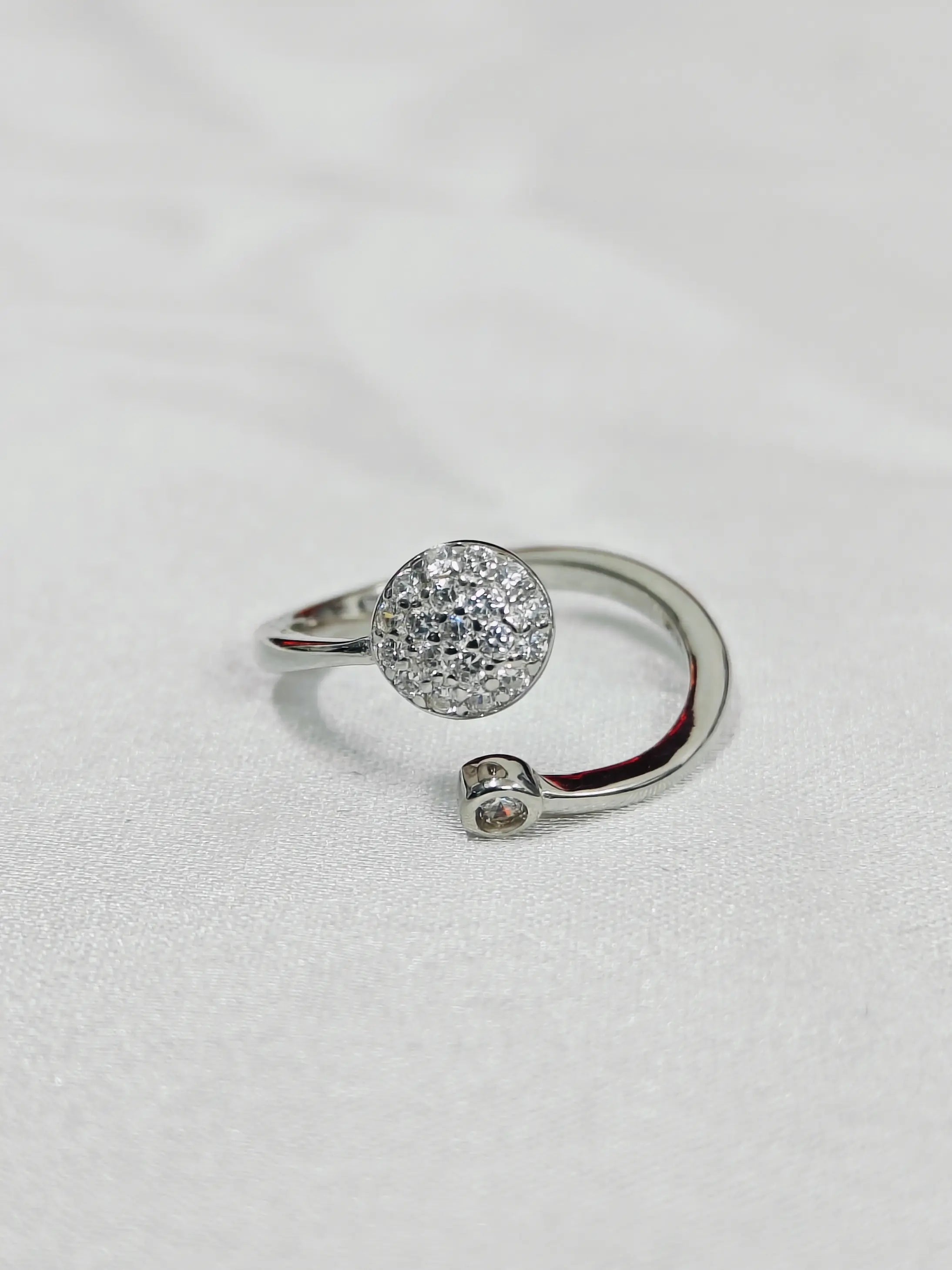 Silver ring with a round, diamond-studded design on a light gray background