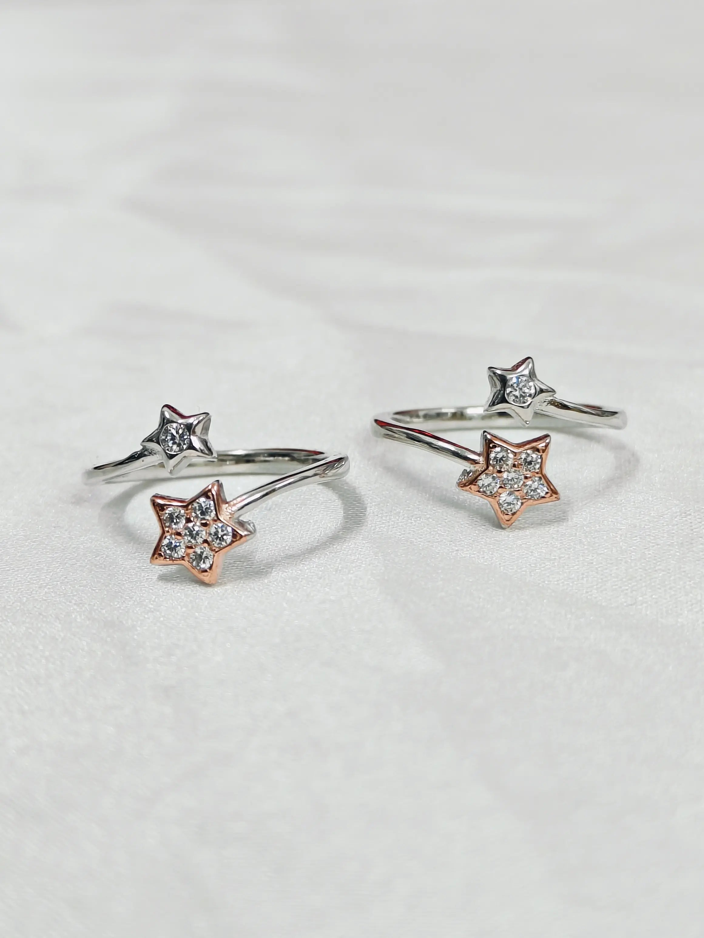 Star-shaped silver and rose gold rings with clear gemstones on a light gray background