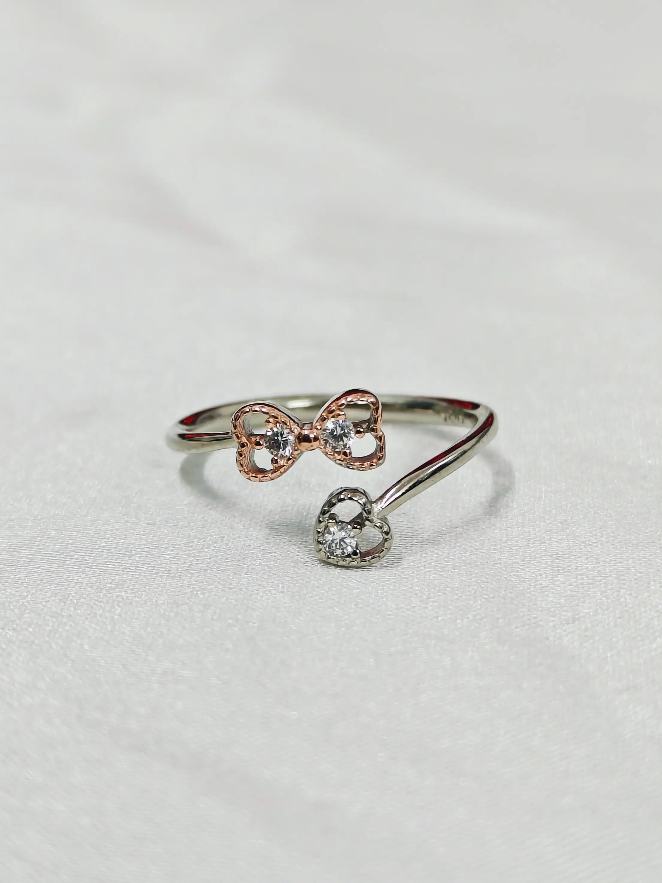 Silver bow-shaped ring with a heart charm on a light gray background