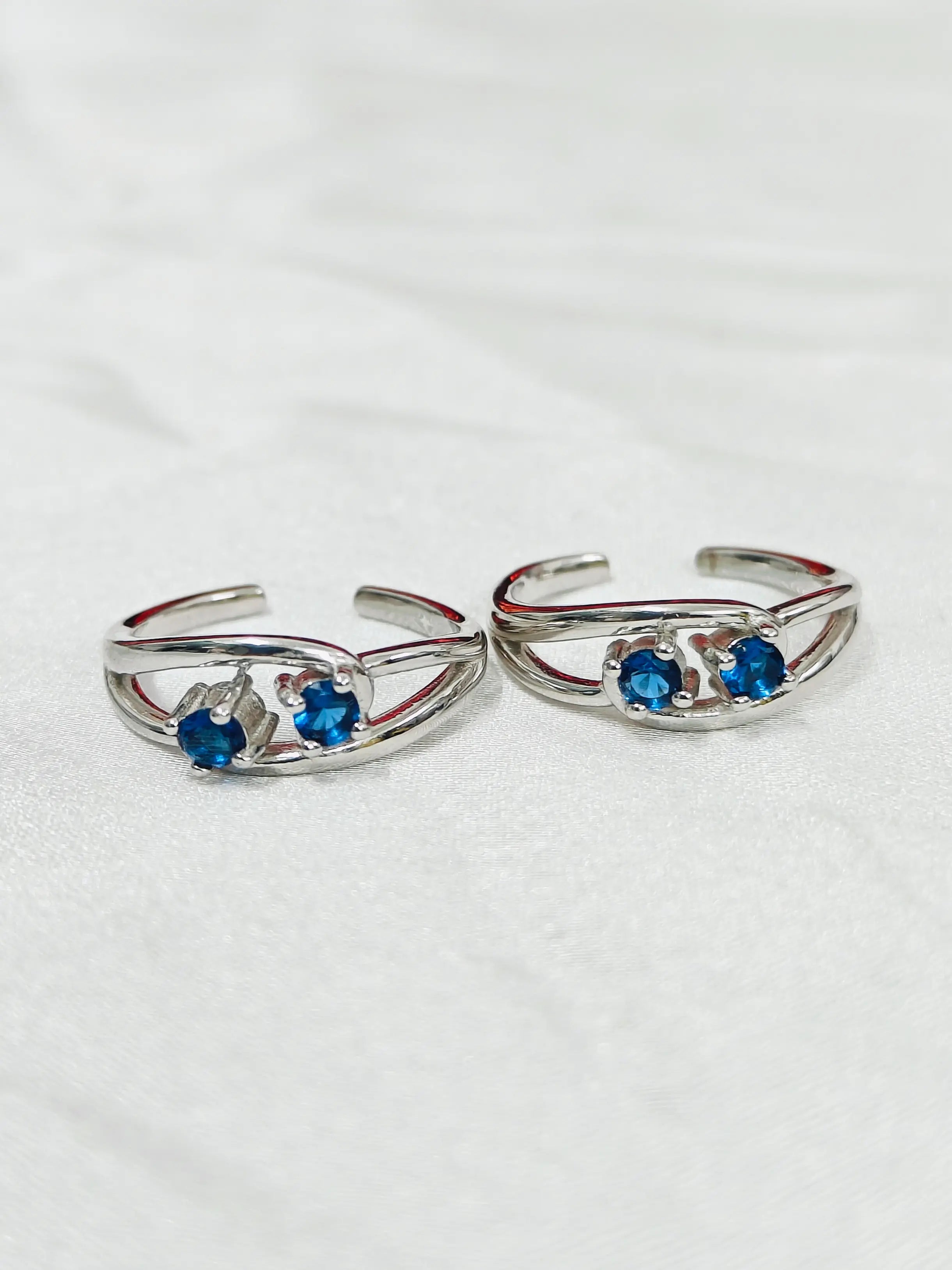 Pair of silver open rings with blue gemstones on a white background