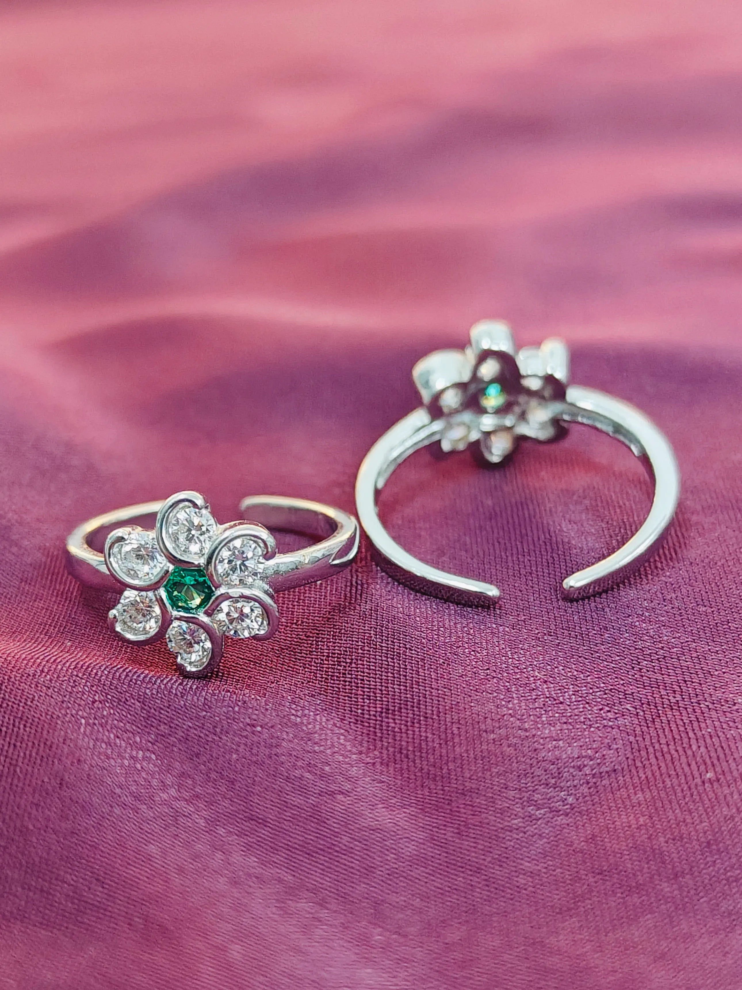 Two silver rings with floral designs and gemstones on a pink fabric background