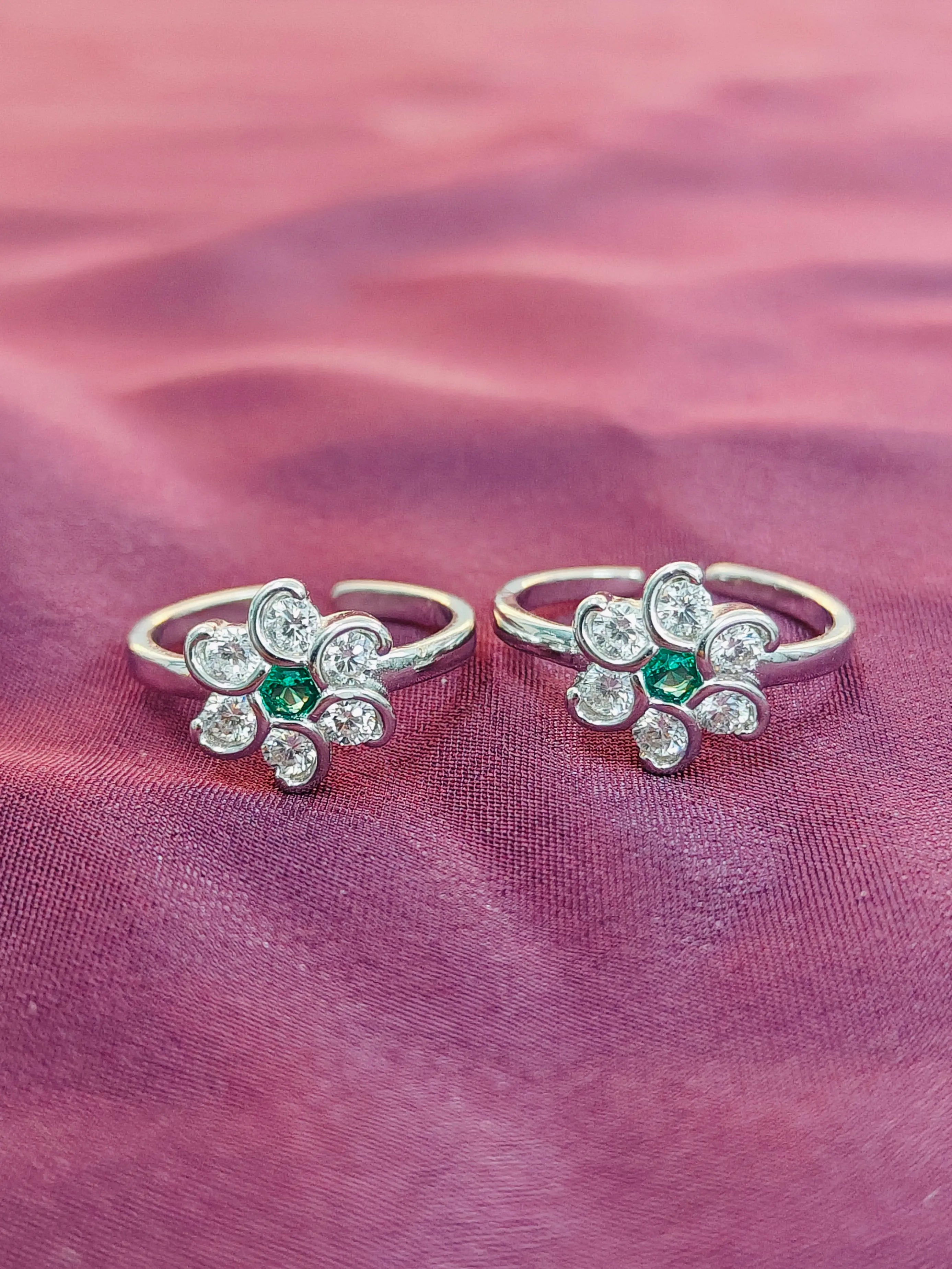 Two silver rings with emerald stones on a pink fabric background