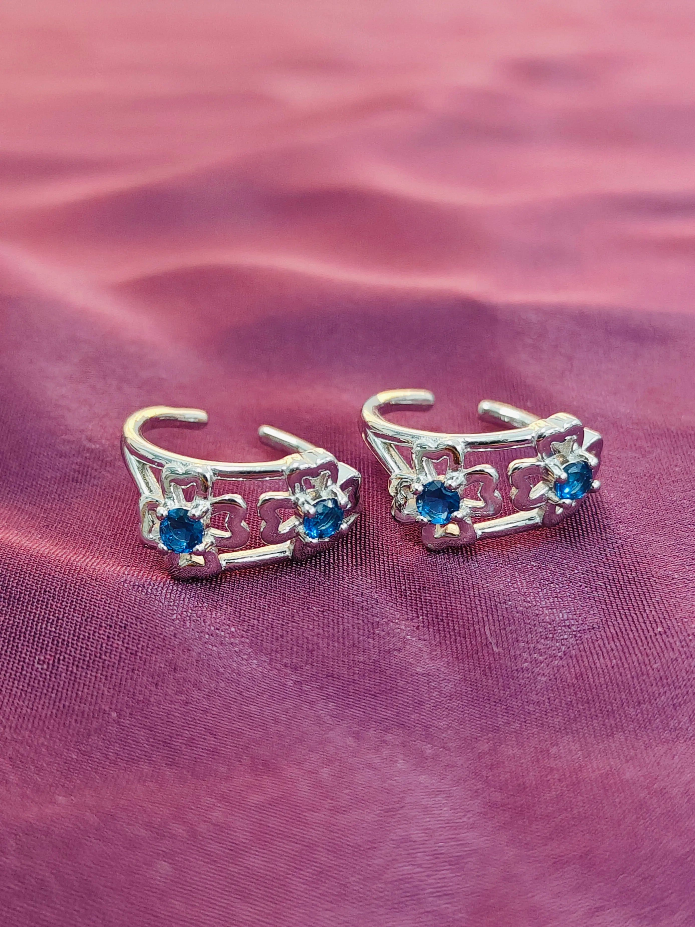 Silver toe rings with blue gemstones on a pink fabric background