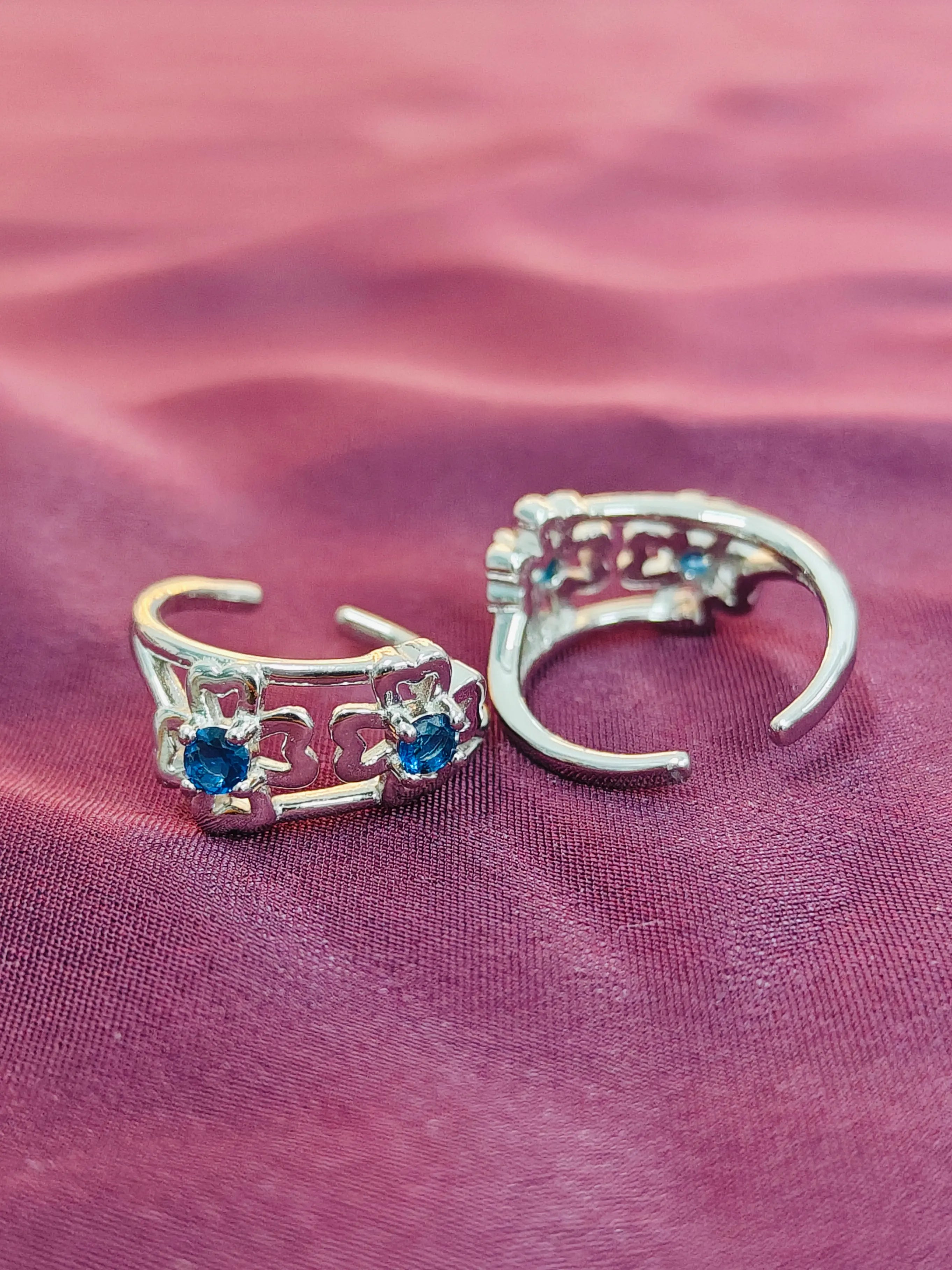 Silver ear cuffs with blue gemstones on a pink fabric background