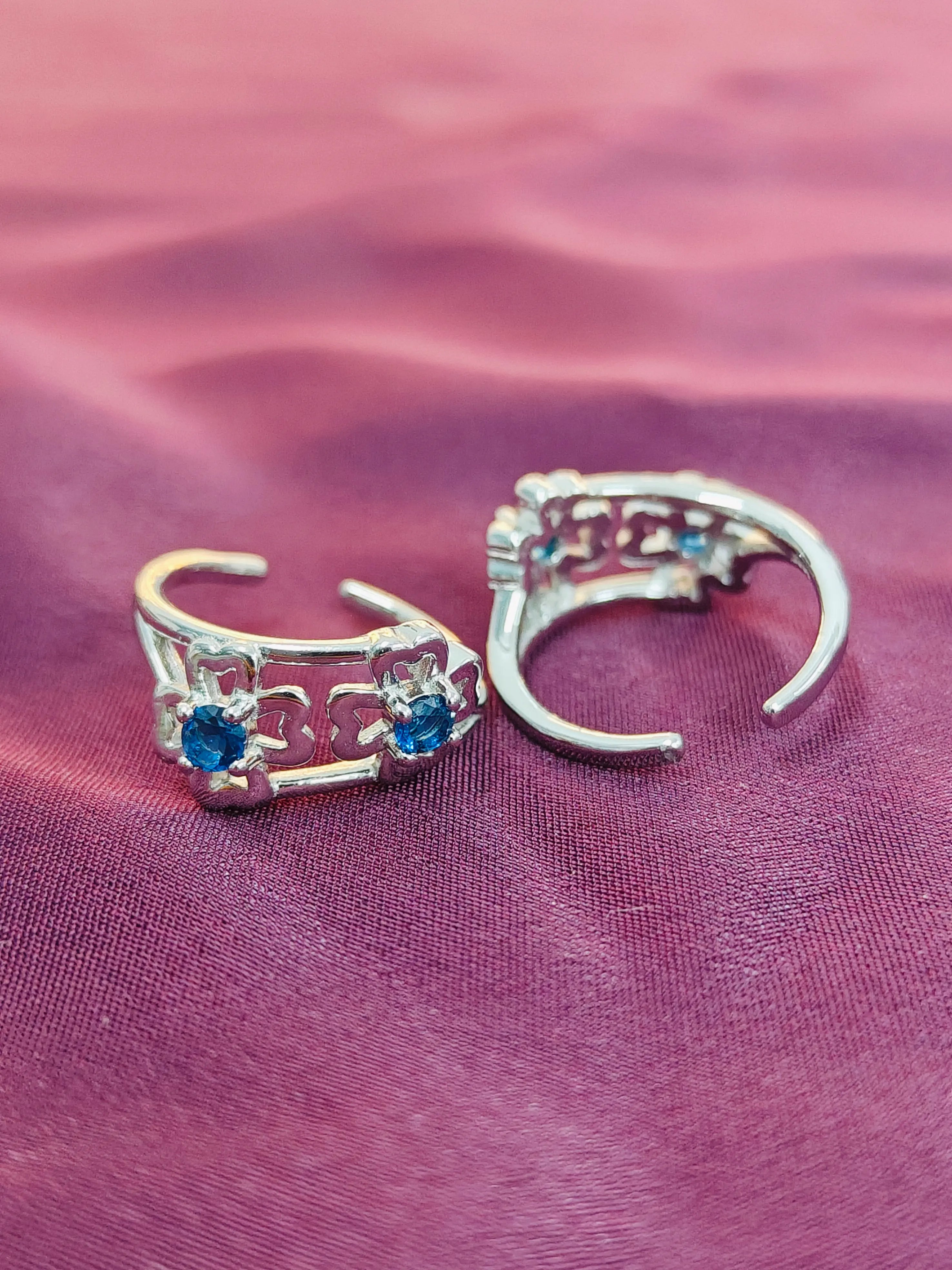 Silver ear cuffs with blue gemstones on a pink fabric background