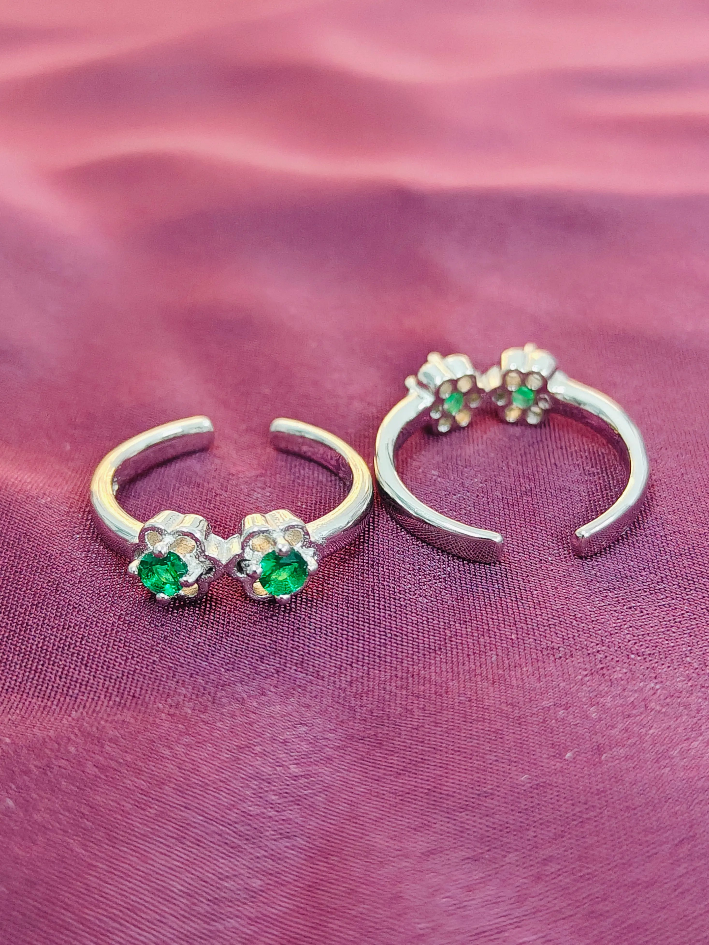 Silver nose rings with green gemstones on a pink fabric background