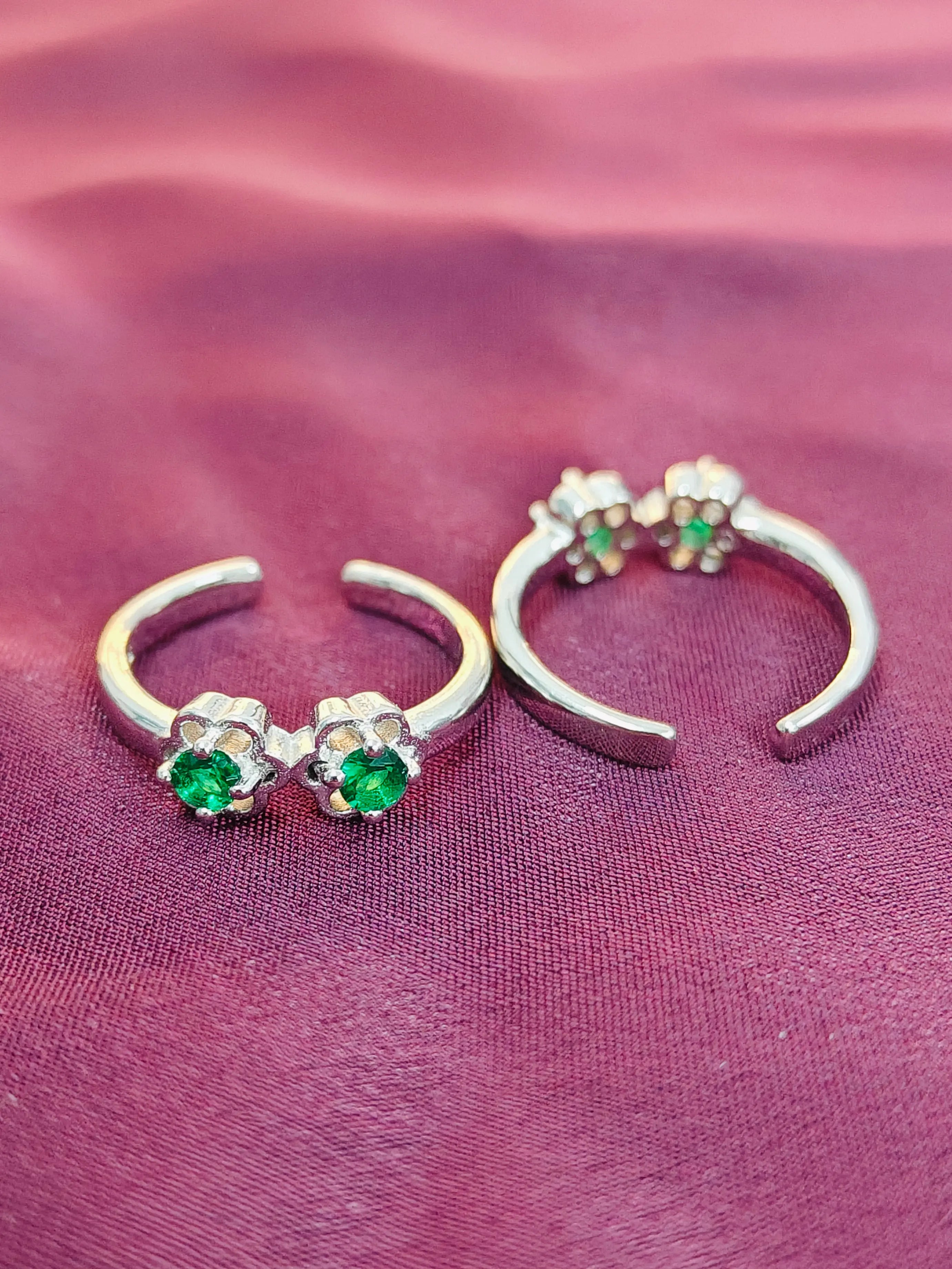 Silver hoop earrings with green gemstones on a pink fabric background