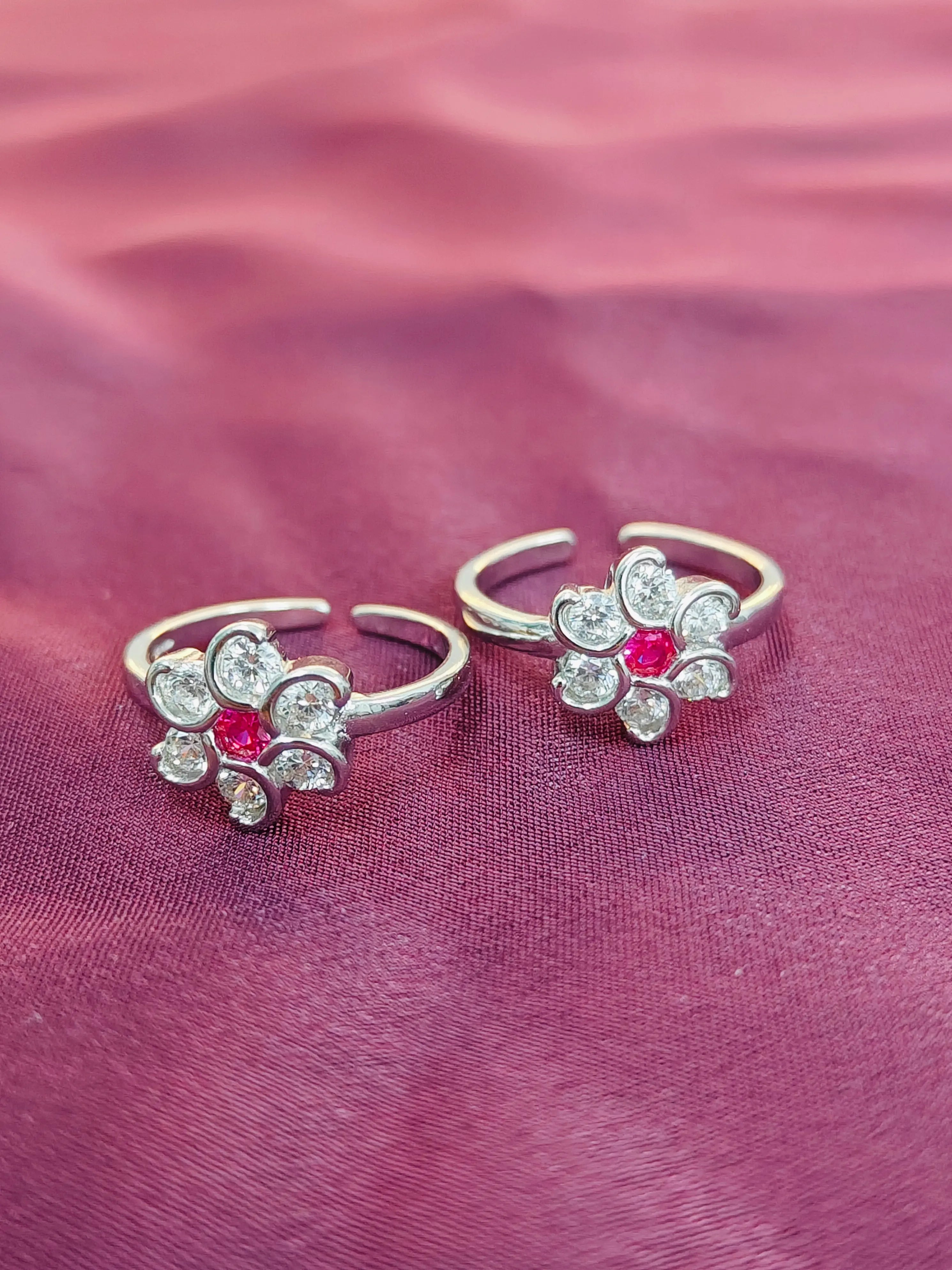 Two silver floral rings with red gemstones on a pink fabric background