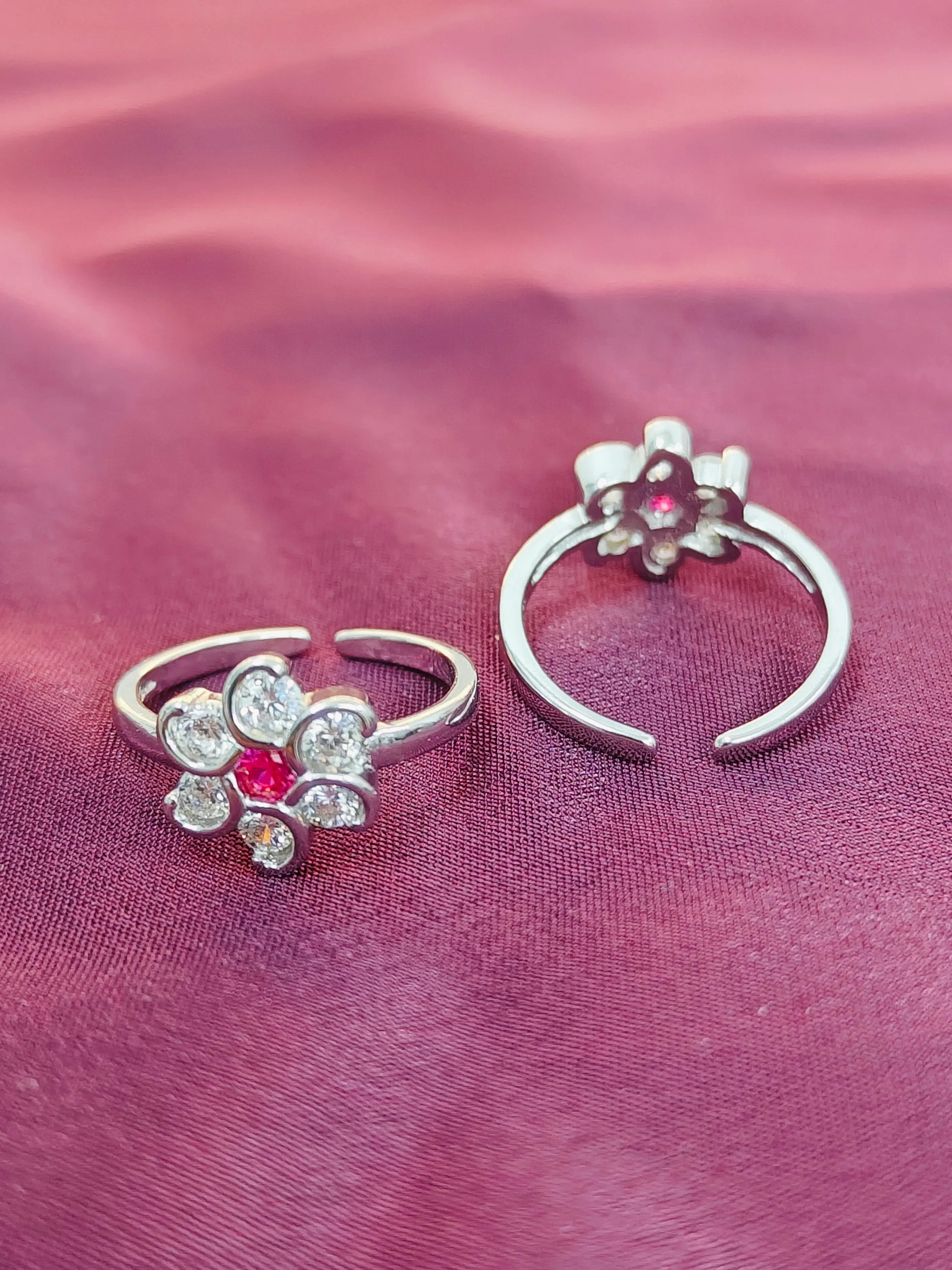 Two silver floral ear cuffs with red gemstones on a pink fabric background