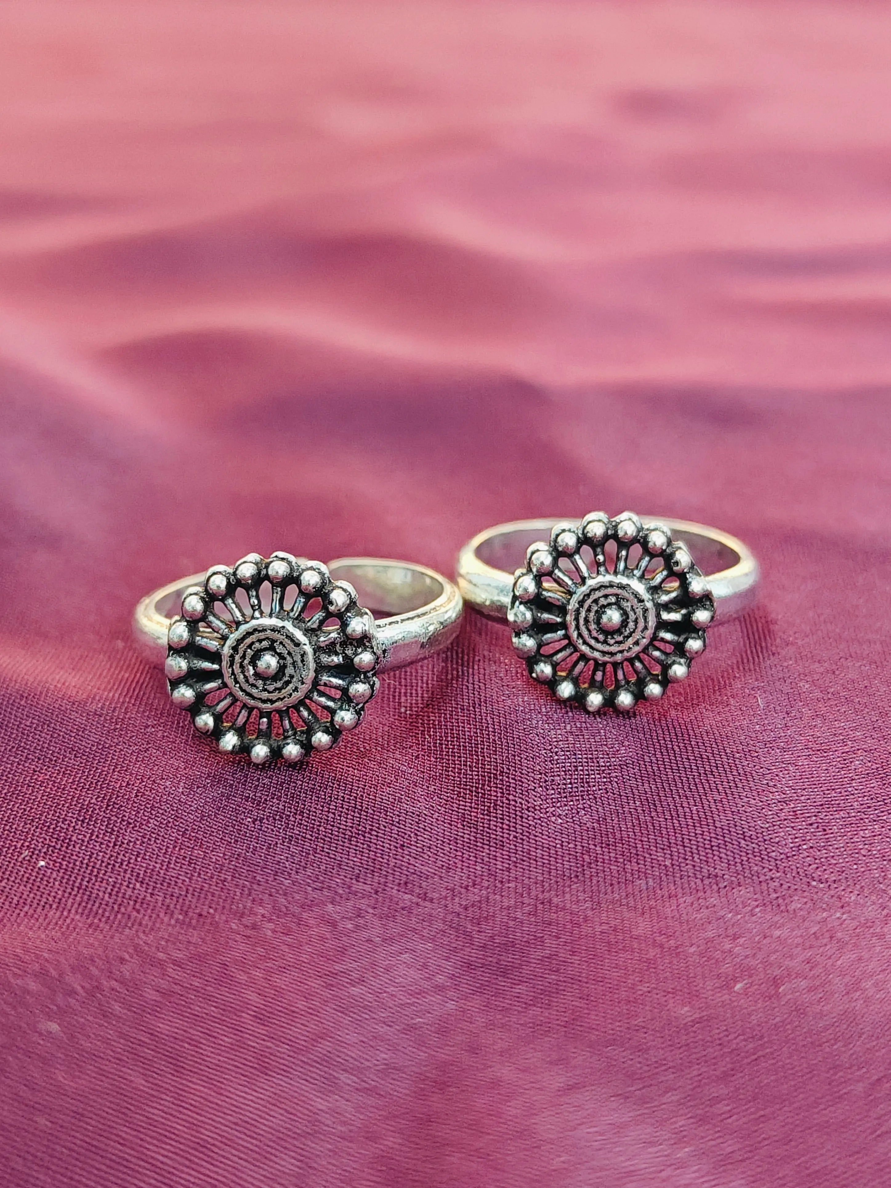 Two silver rings with decorative designs on a pink fabric background
