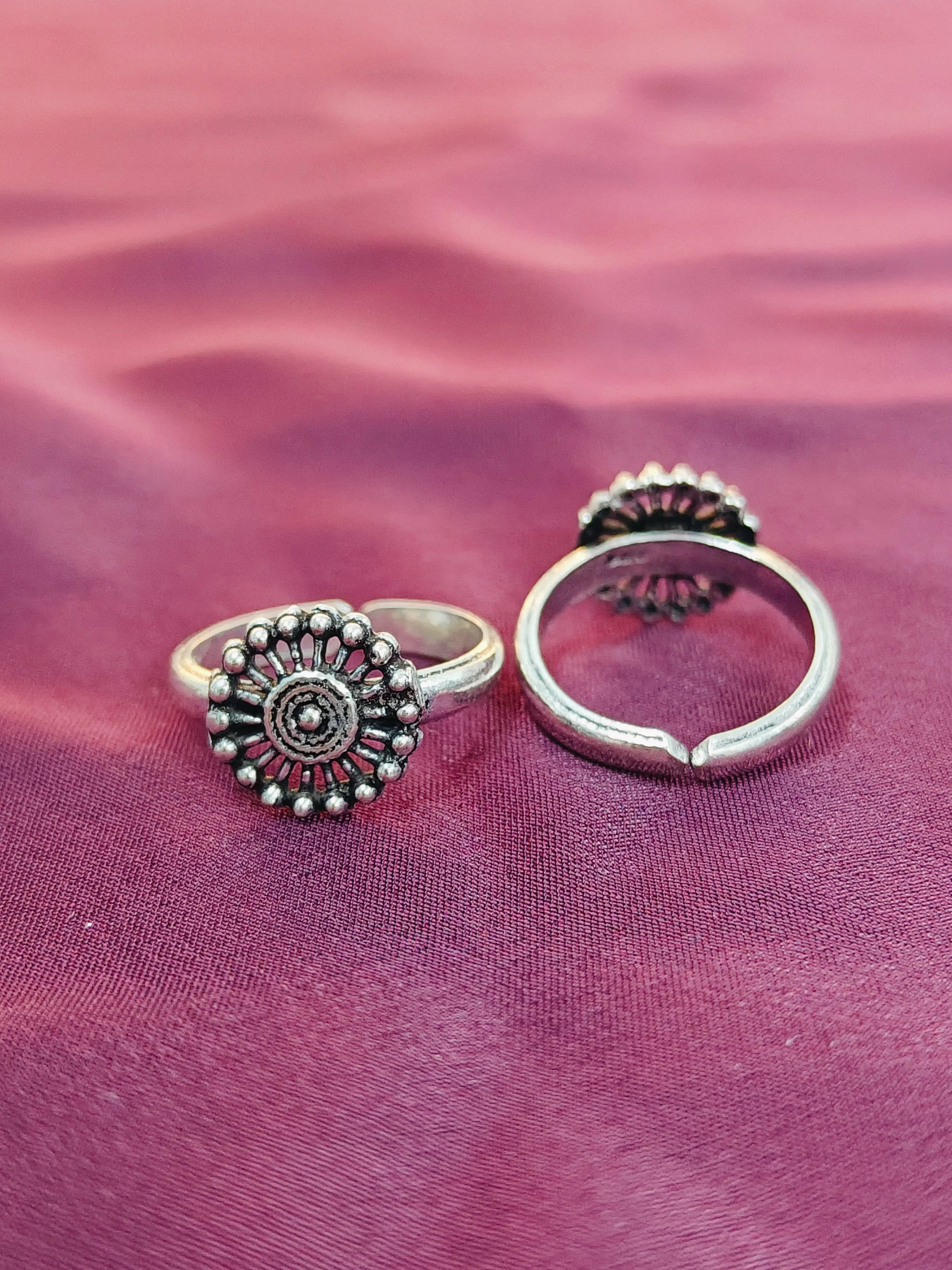 Two silver rings with intricate designs on a purple fabric background