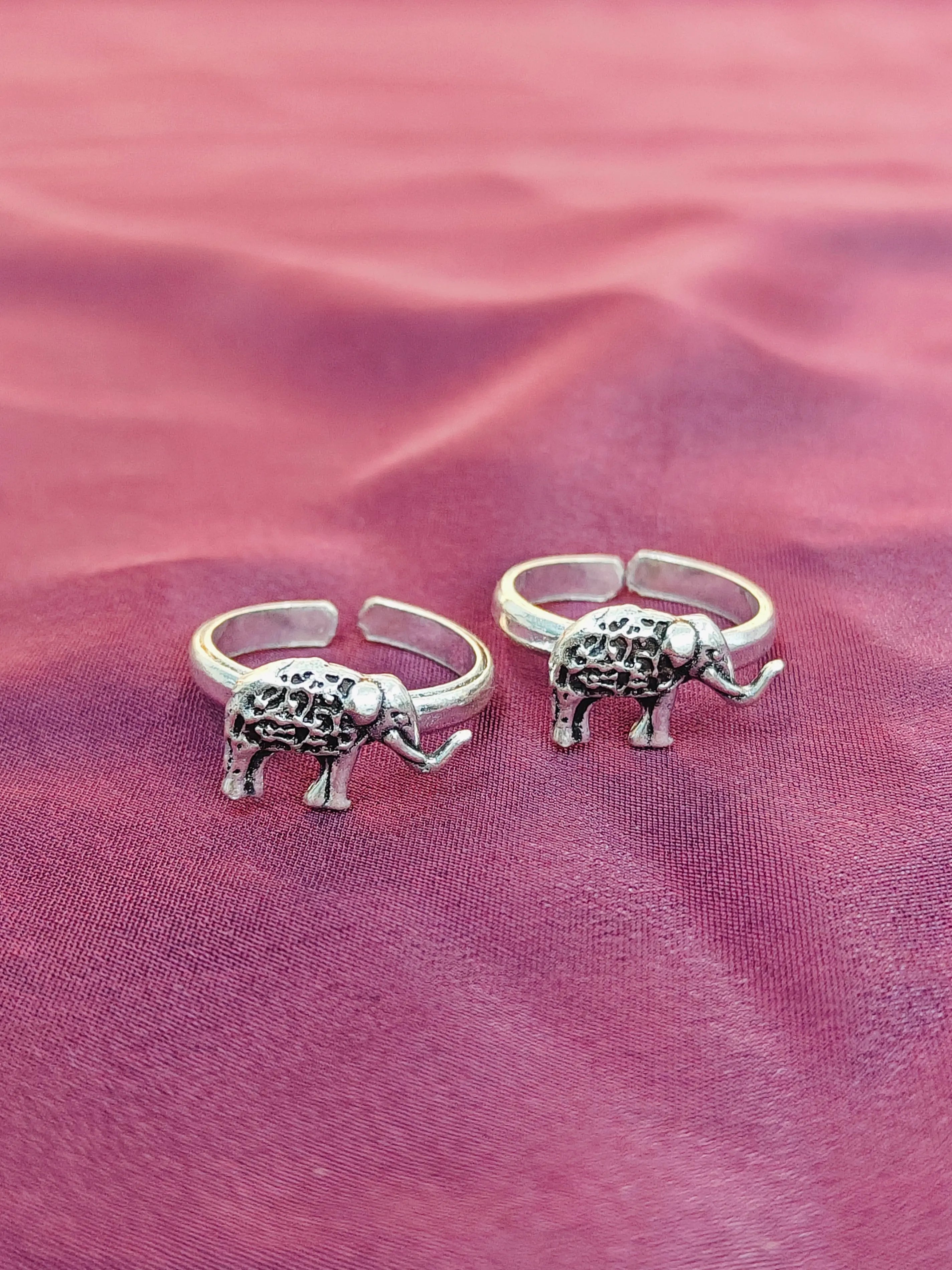 Two silver elephant-shaped rings on a pink fabric background