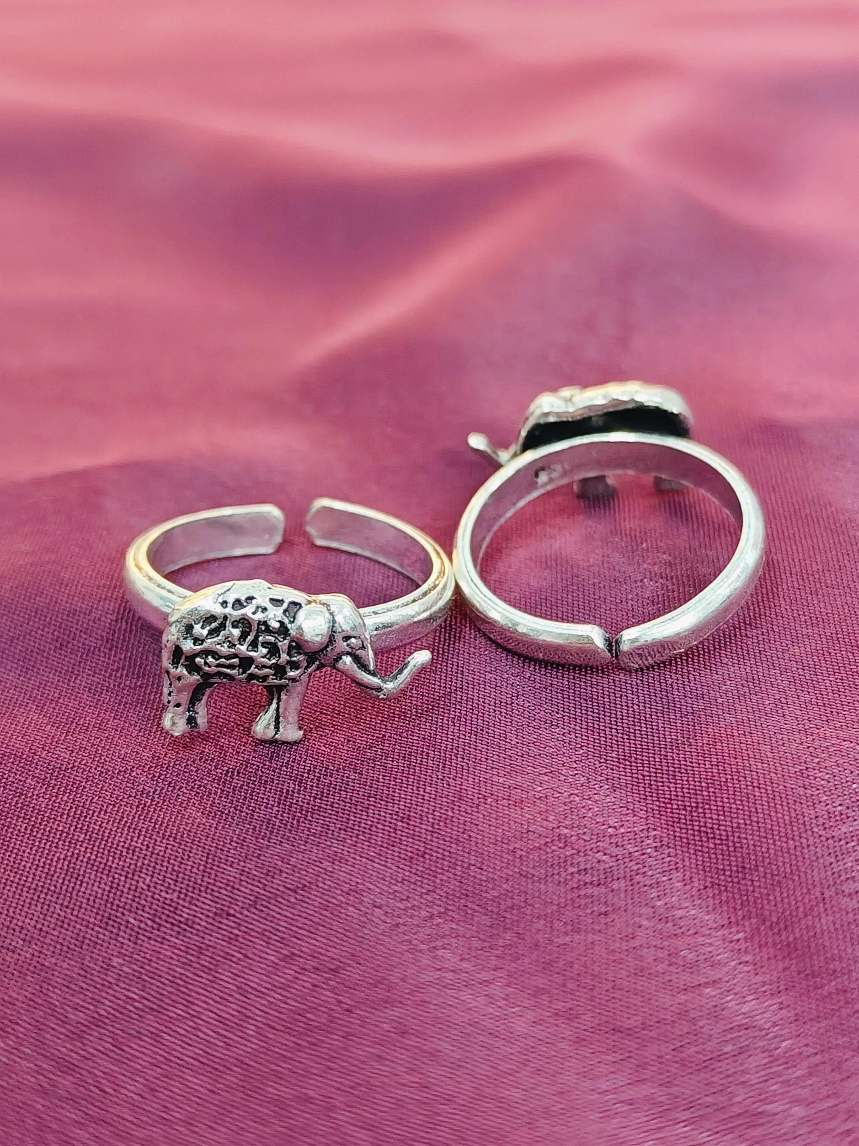 Silver elephant ring and hoop earring on a pink fabric background