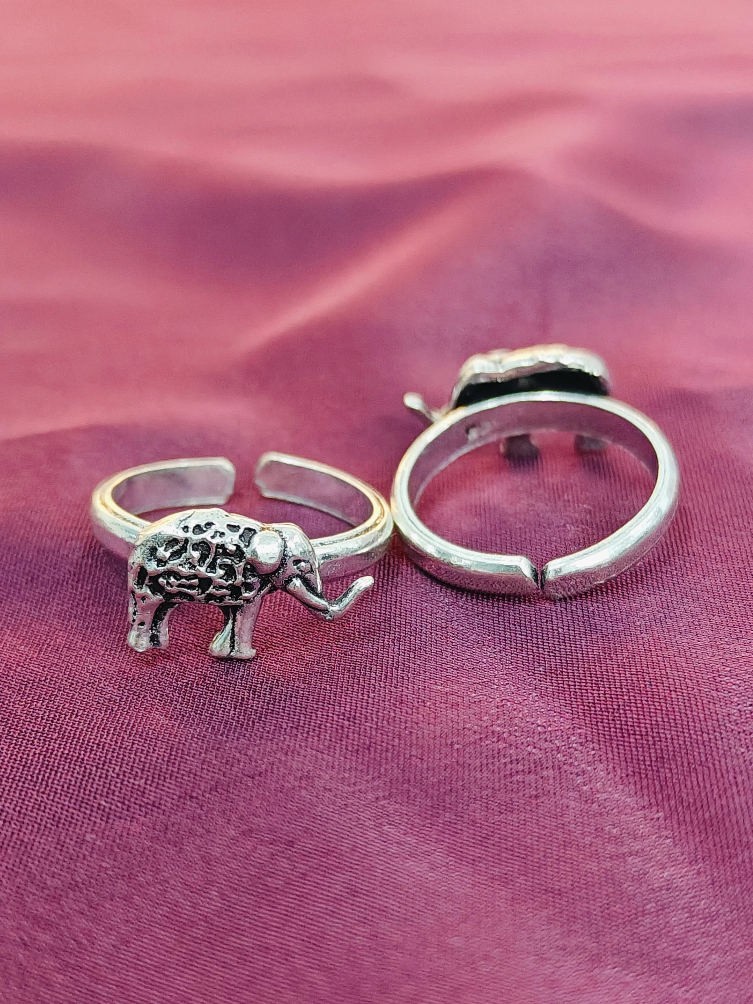 Silver elephant ring and hoop earring on a pink fabric background
