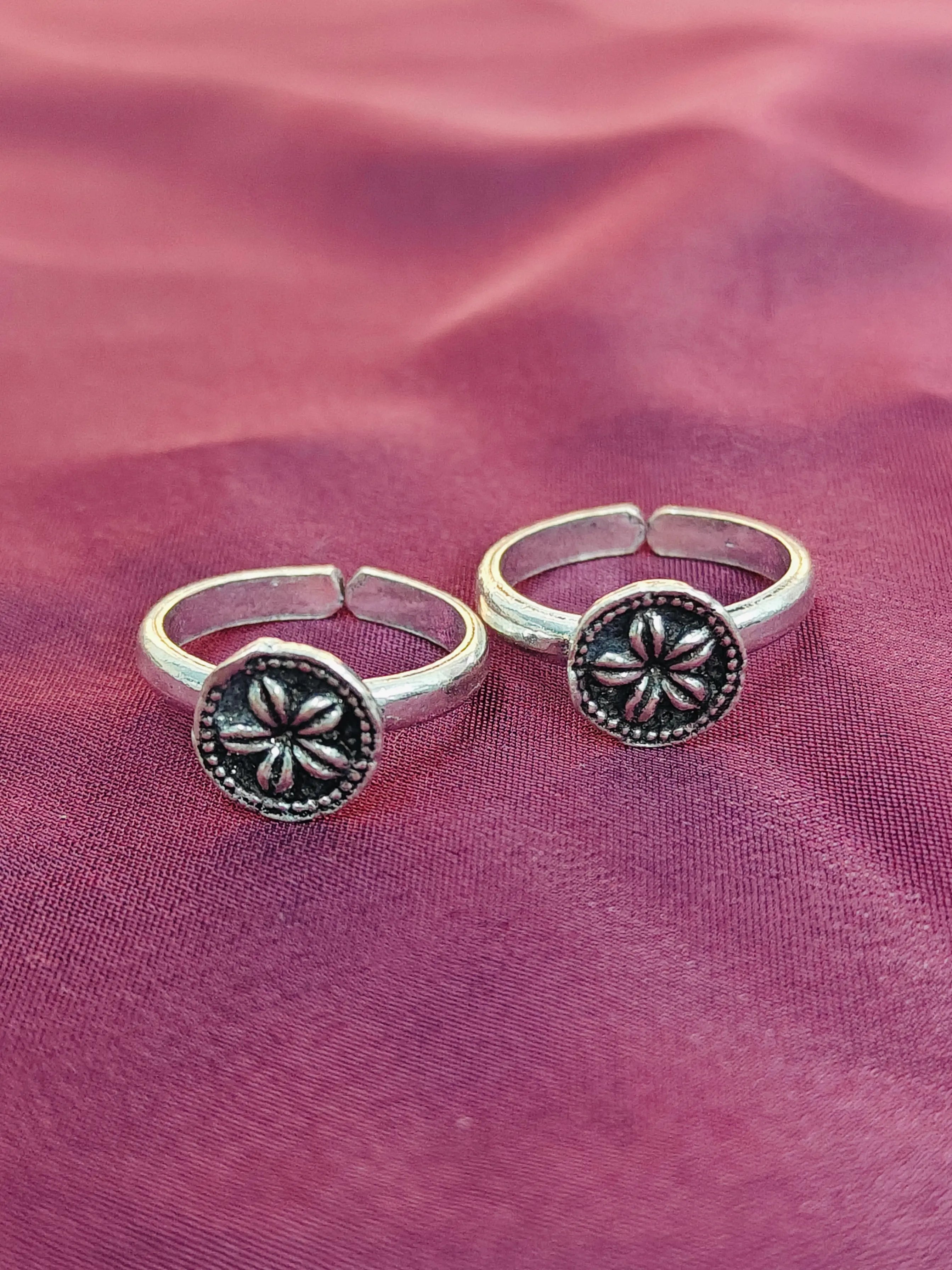 Two silver rings with floral designs on a pink fabric background