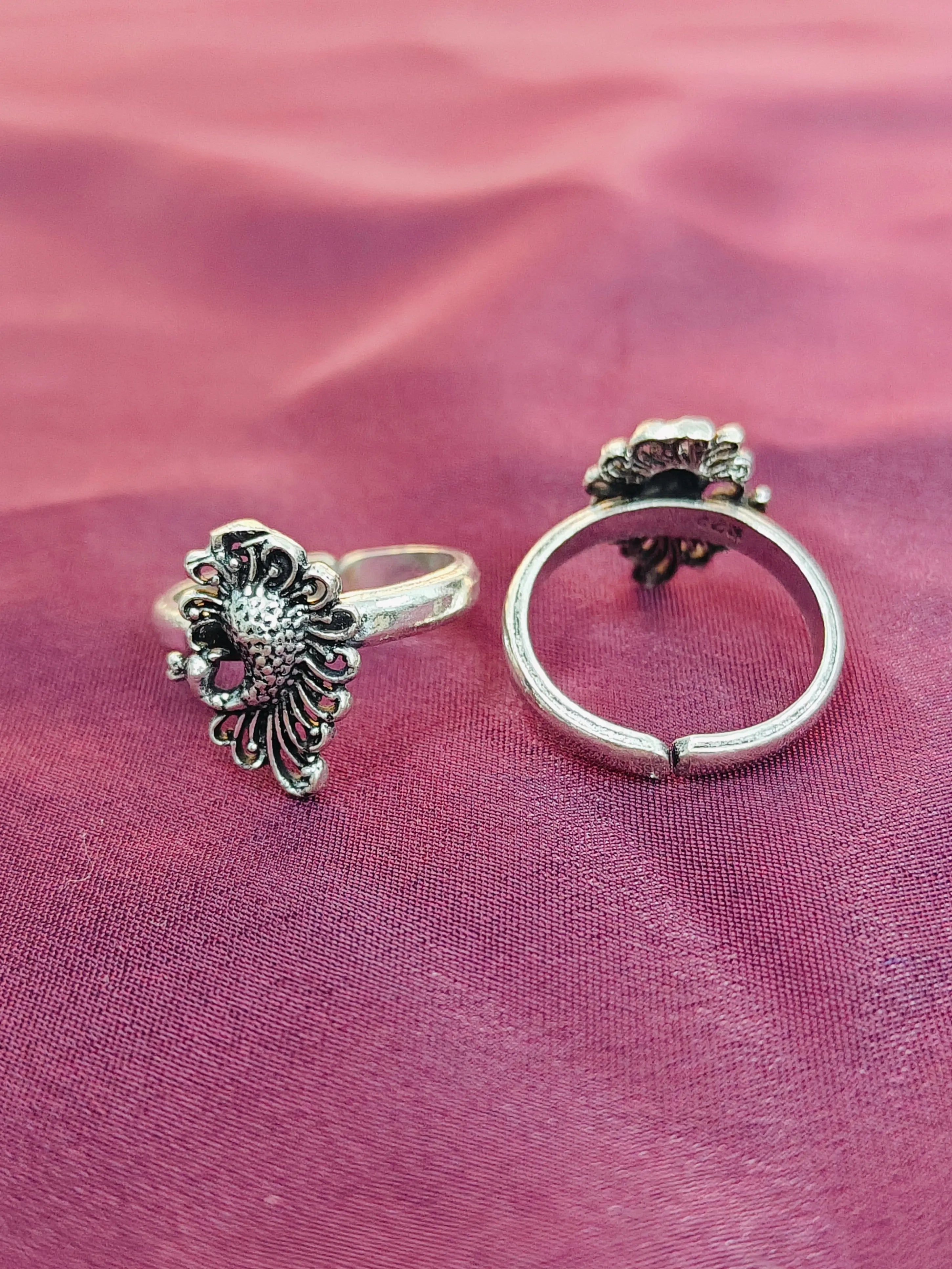 Two silver rings with decorative designs on a pink fabric background