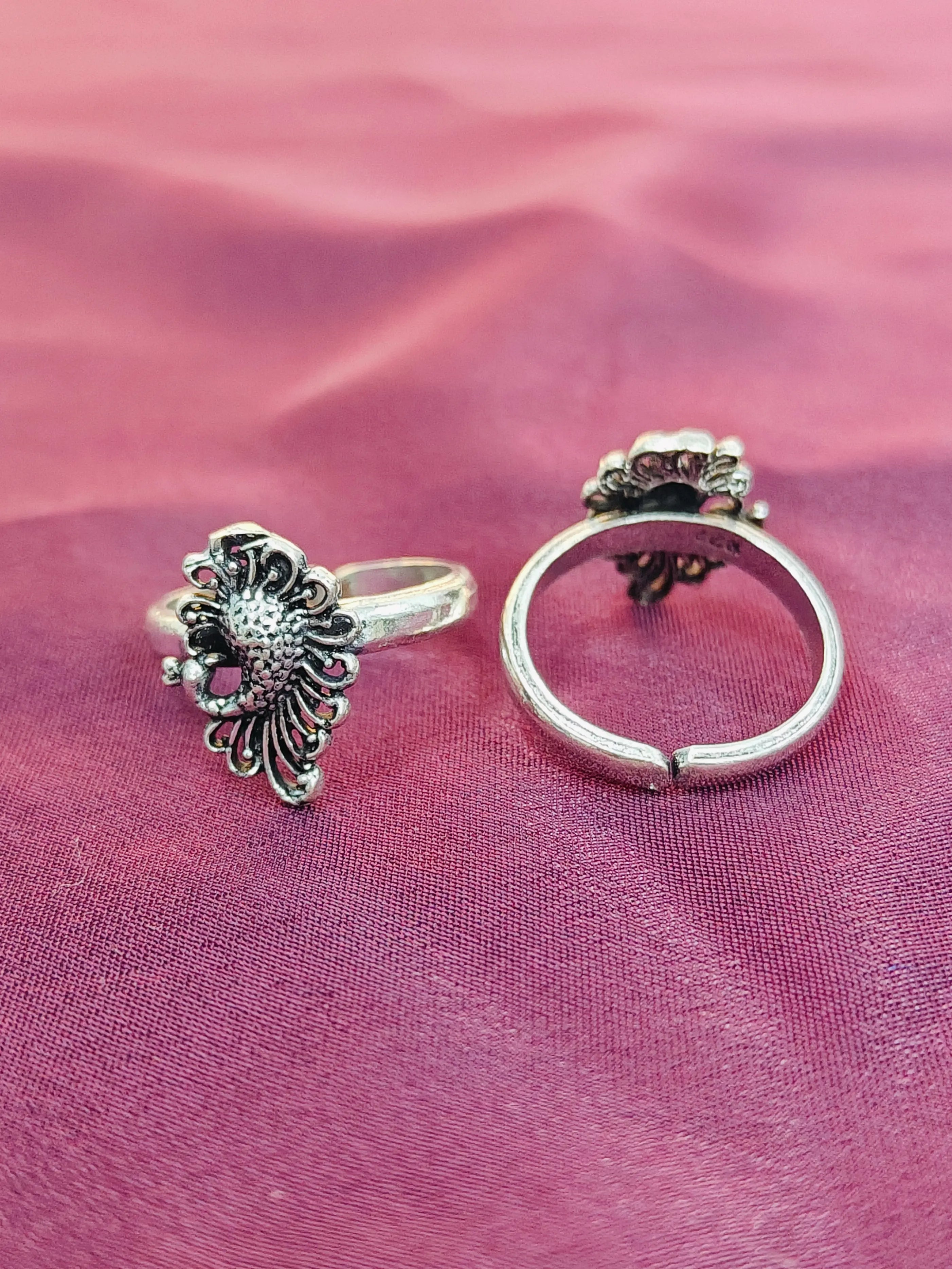 Two silver rings with floral designs on a pink fabric background