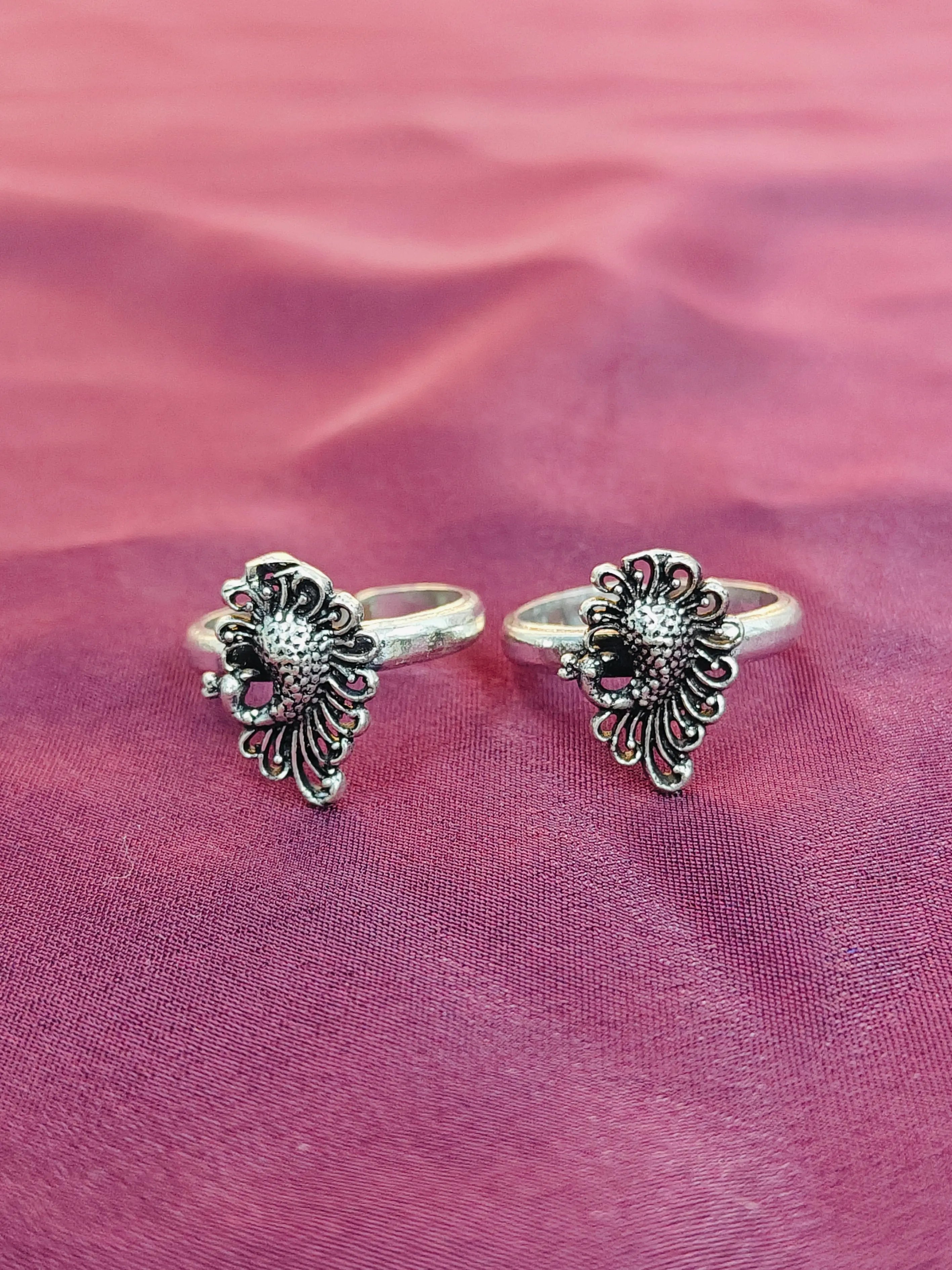Two silver rings with floral designs on a pink fabric background