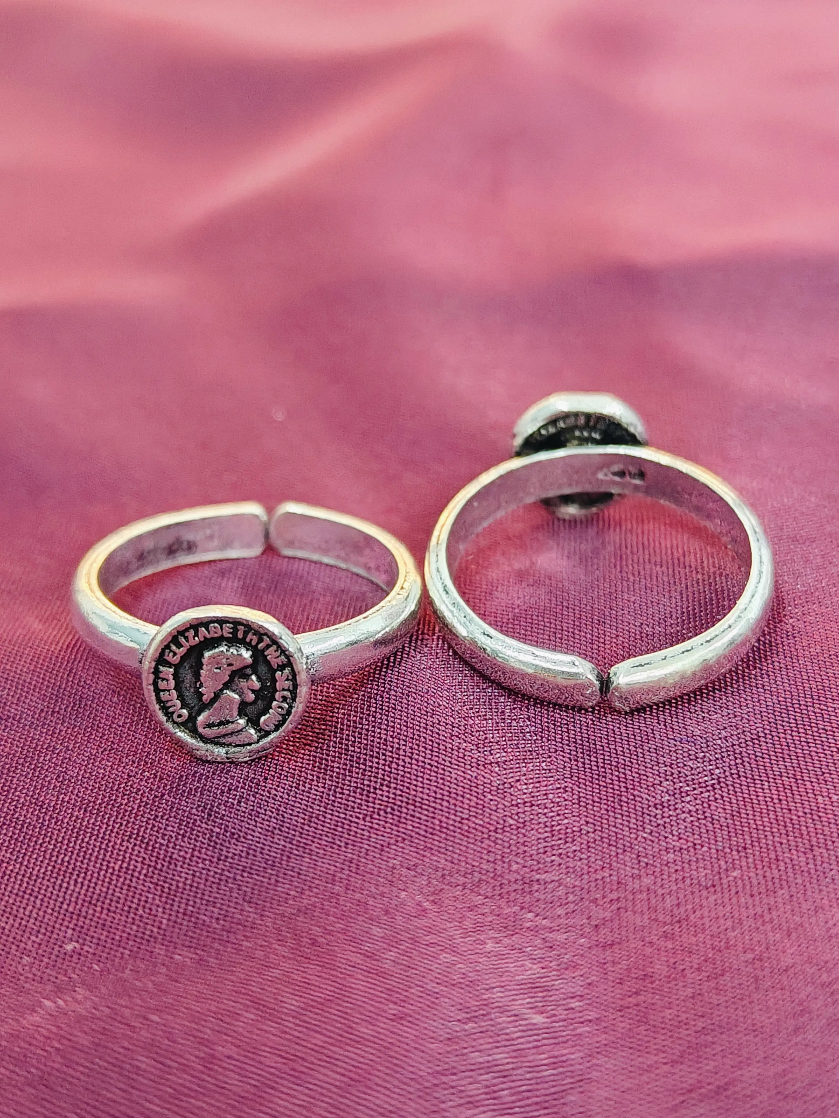 Two silver rings with circular designs on a pink fabric background