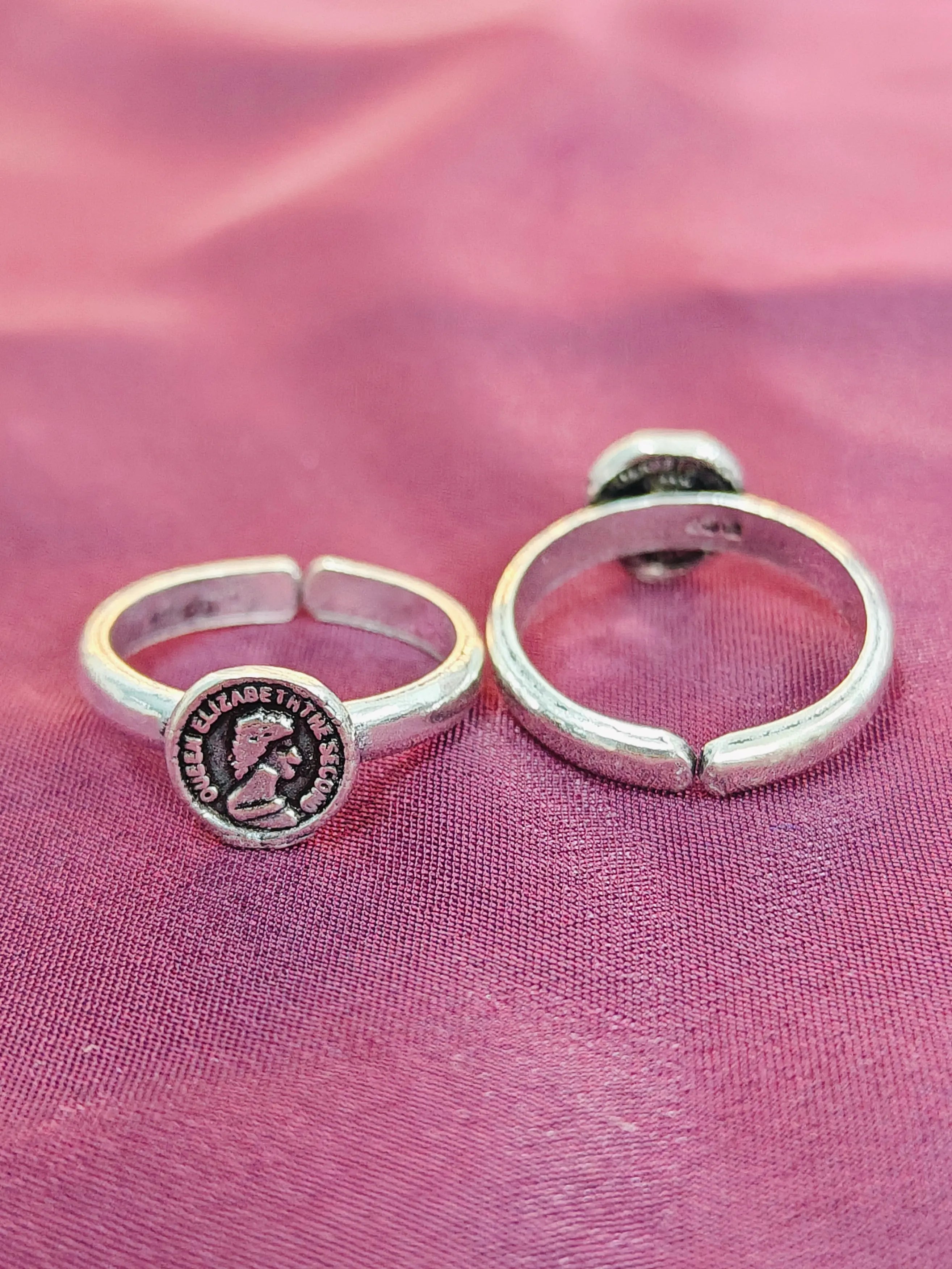 Two silver rings with circular designs on a pink fabric background
