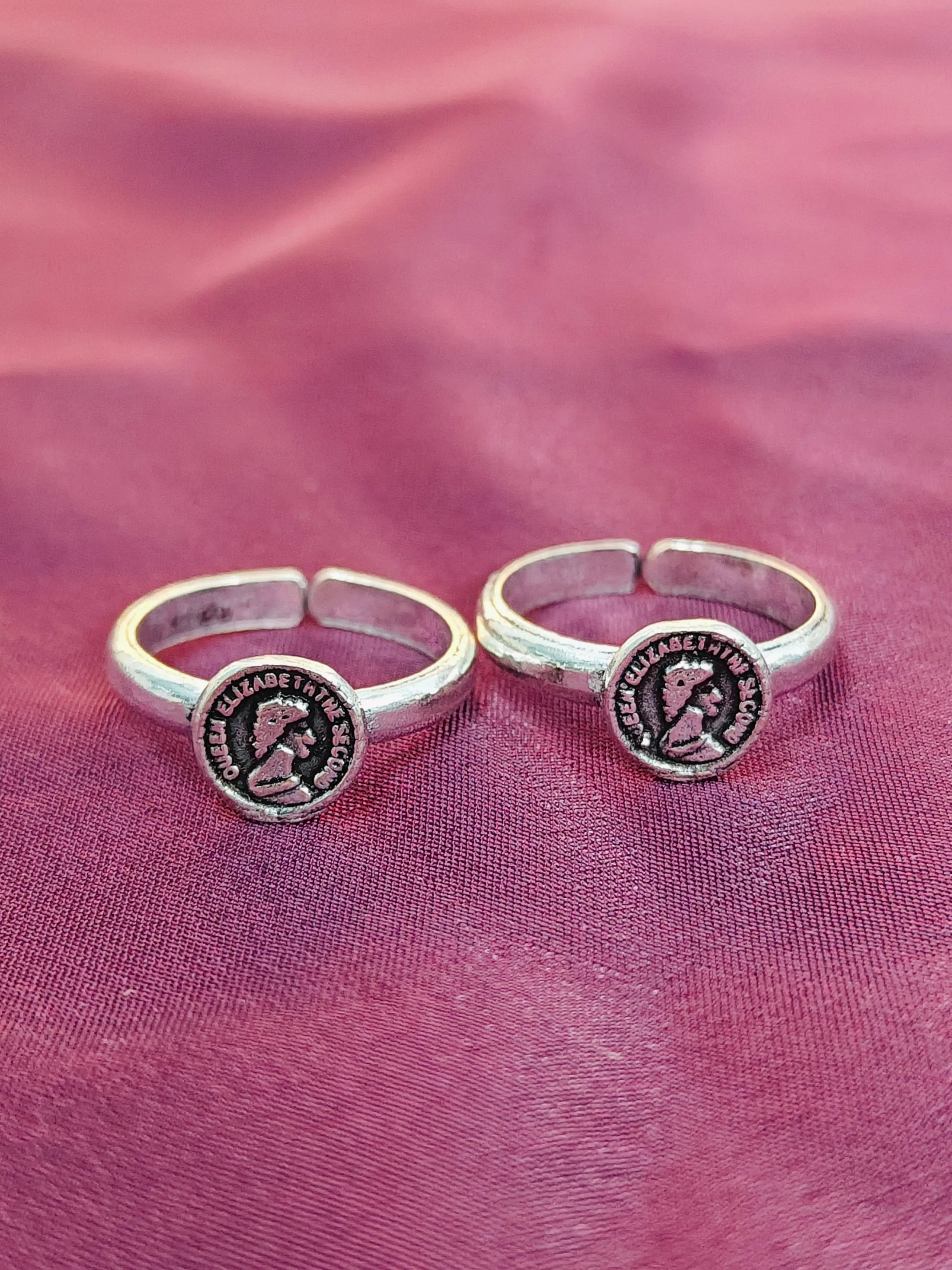 Two silver rings with circular designs on a pink fabric background