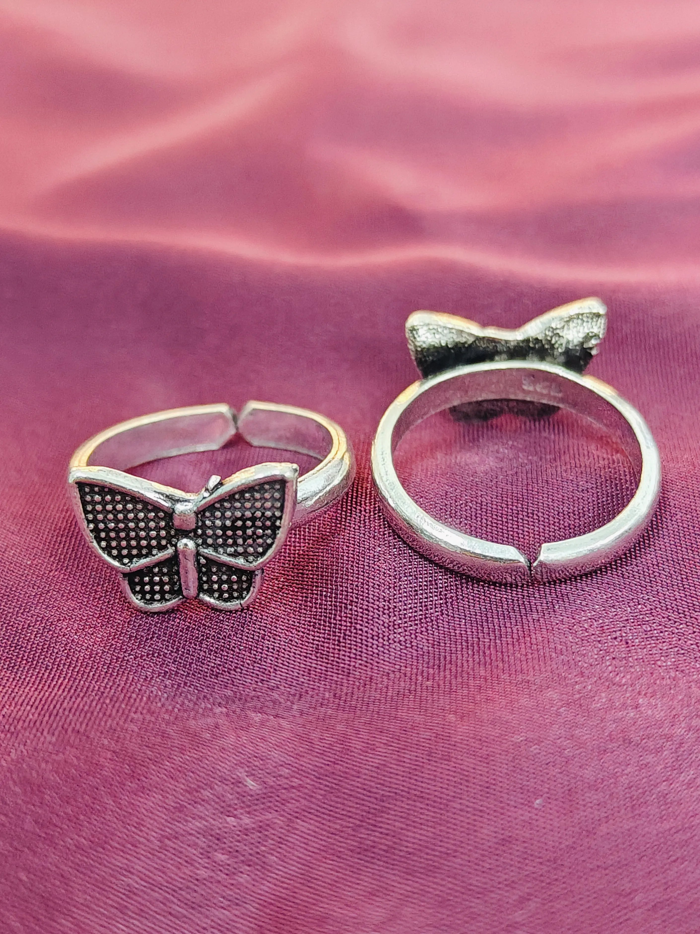 Two silver butterfly-themed rings on a pink fabric background