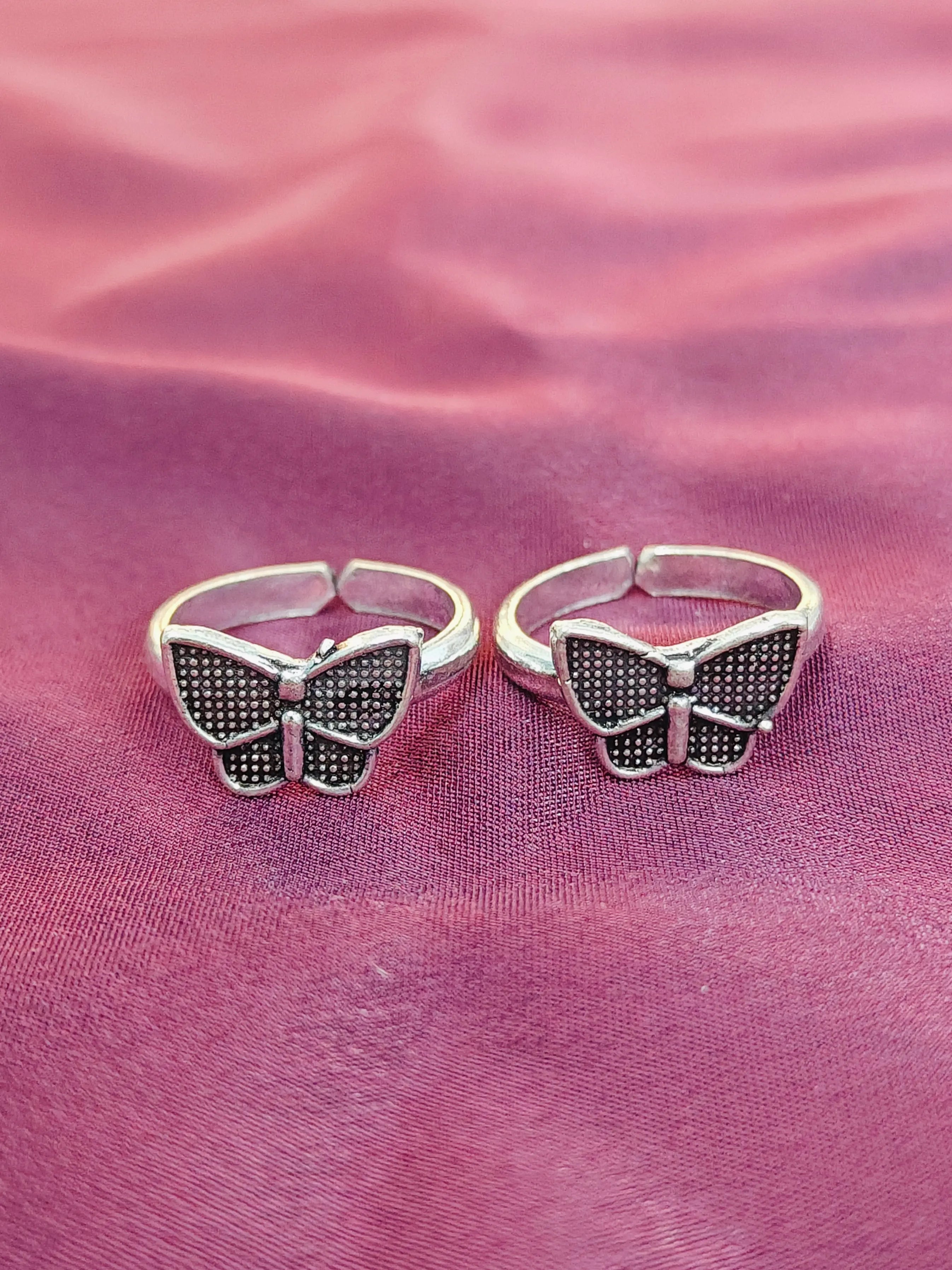 Butterfly-shaped silver rings on a pink fabric background