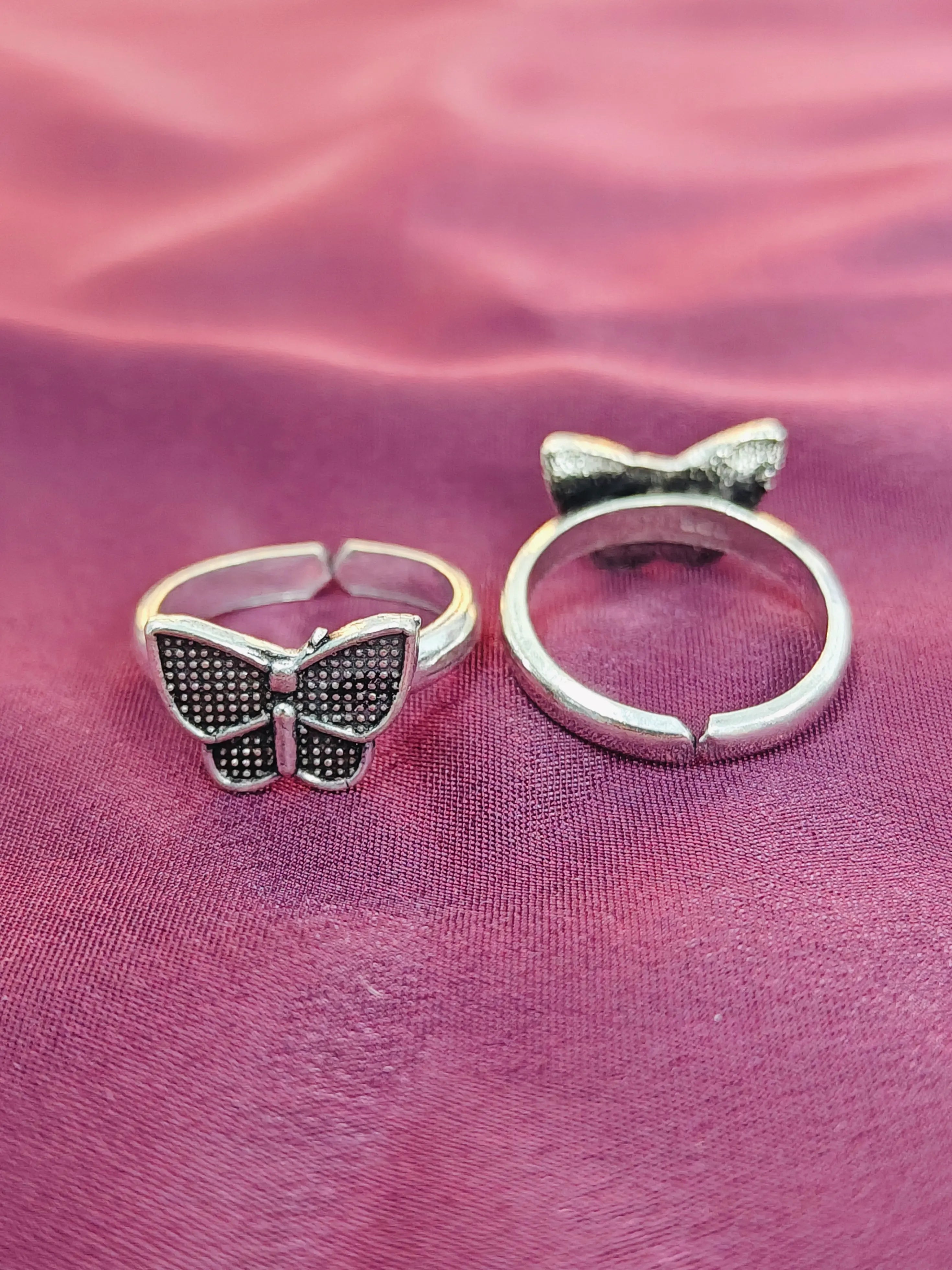 Two butterfly-shaped silver rings on a pink fabric background
