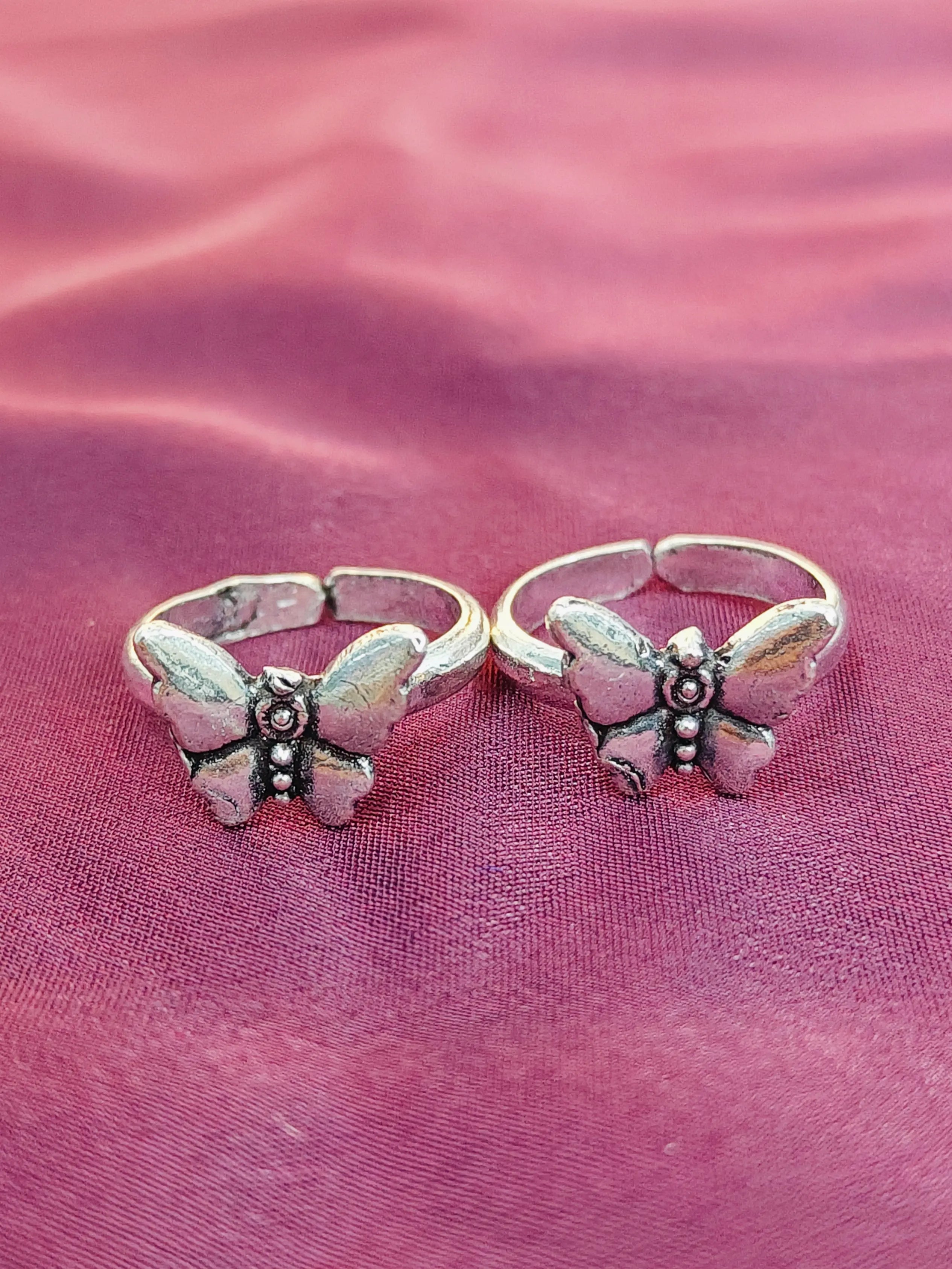 Two butterfly-shaped silver rings on a pink fabric background
