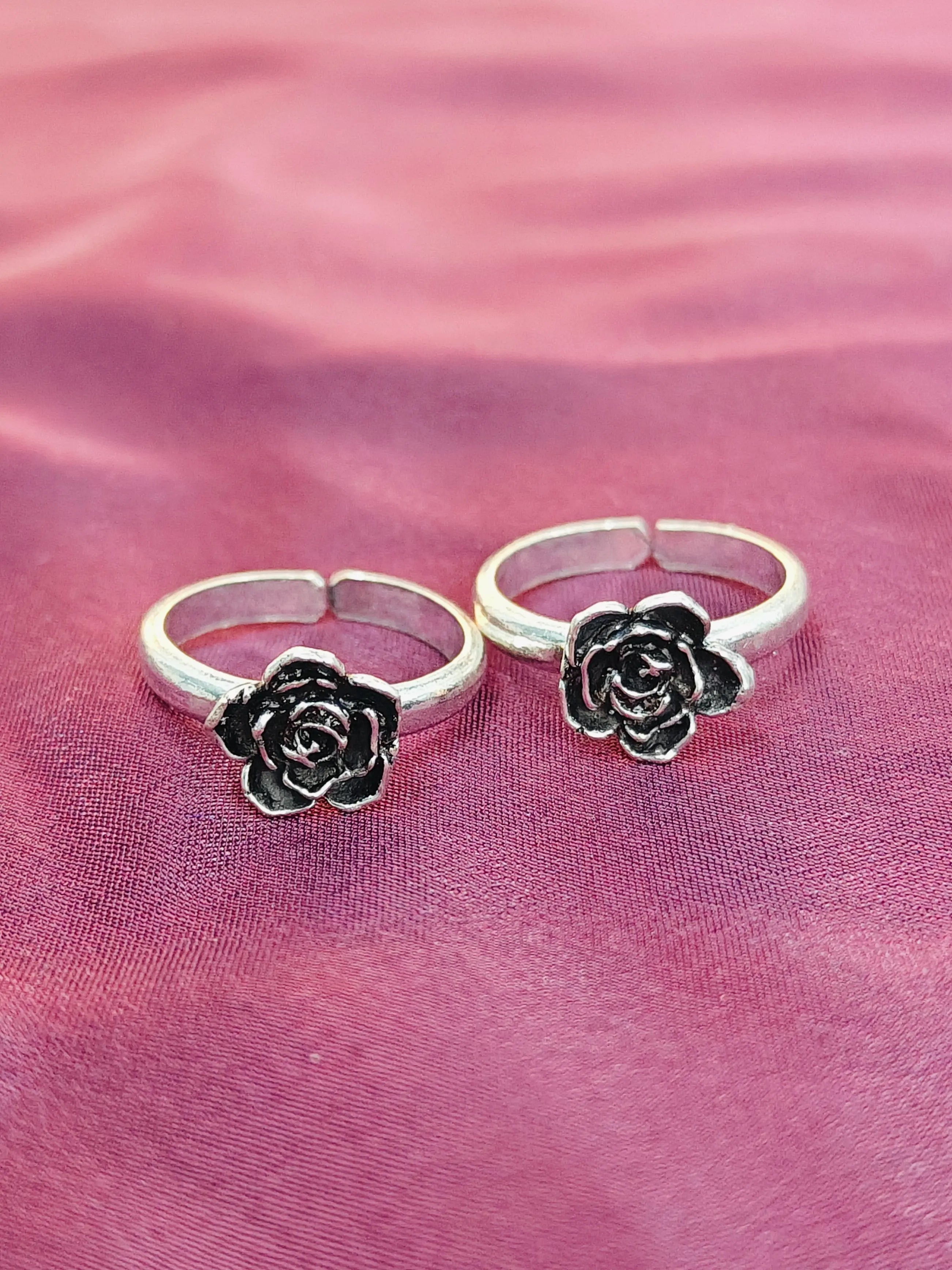 Two silver rings with rose designs on a pink fabric background