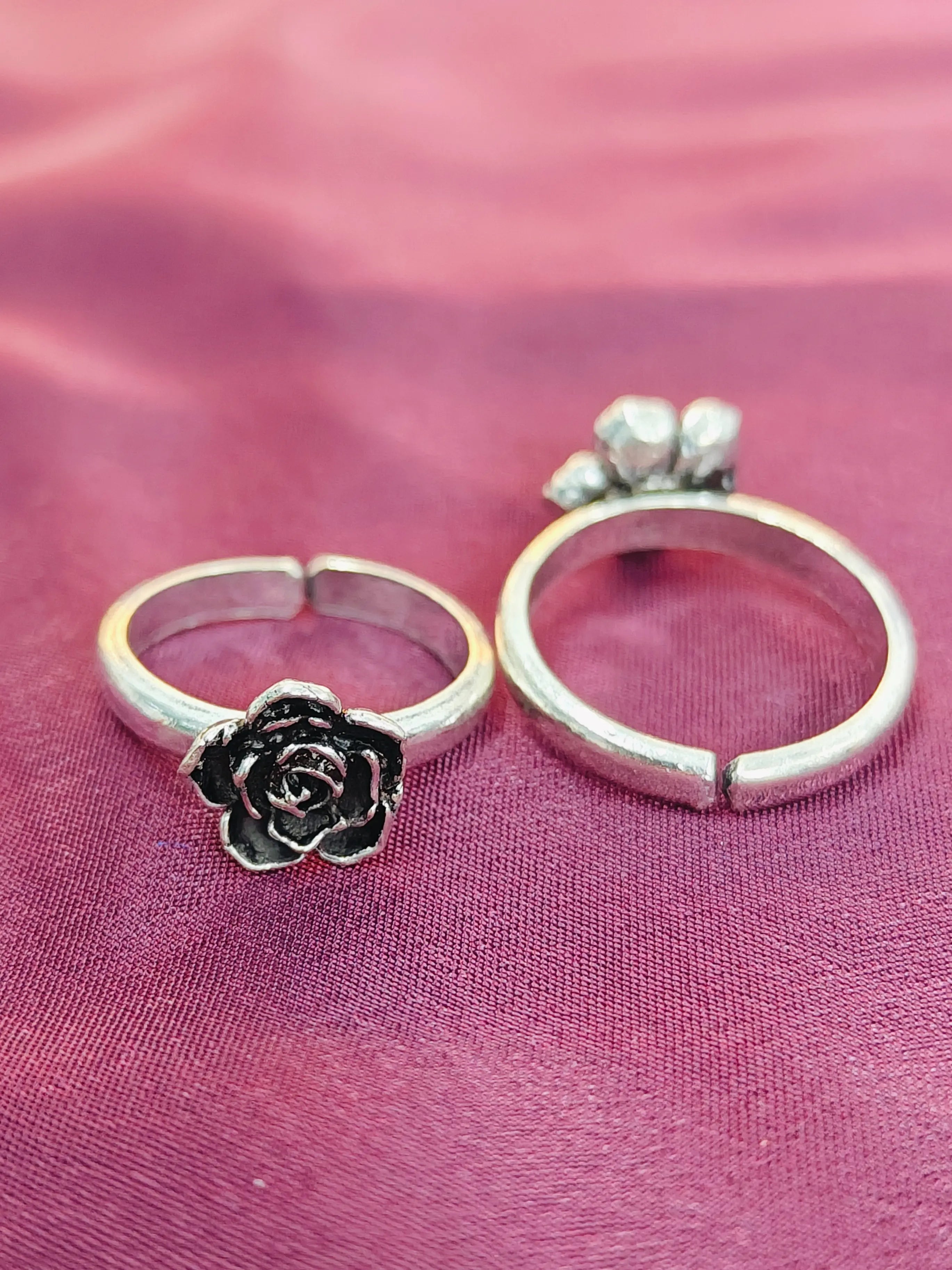 Two silver rings with floral designs on a pink fabric background
