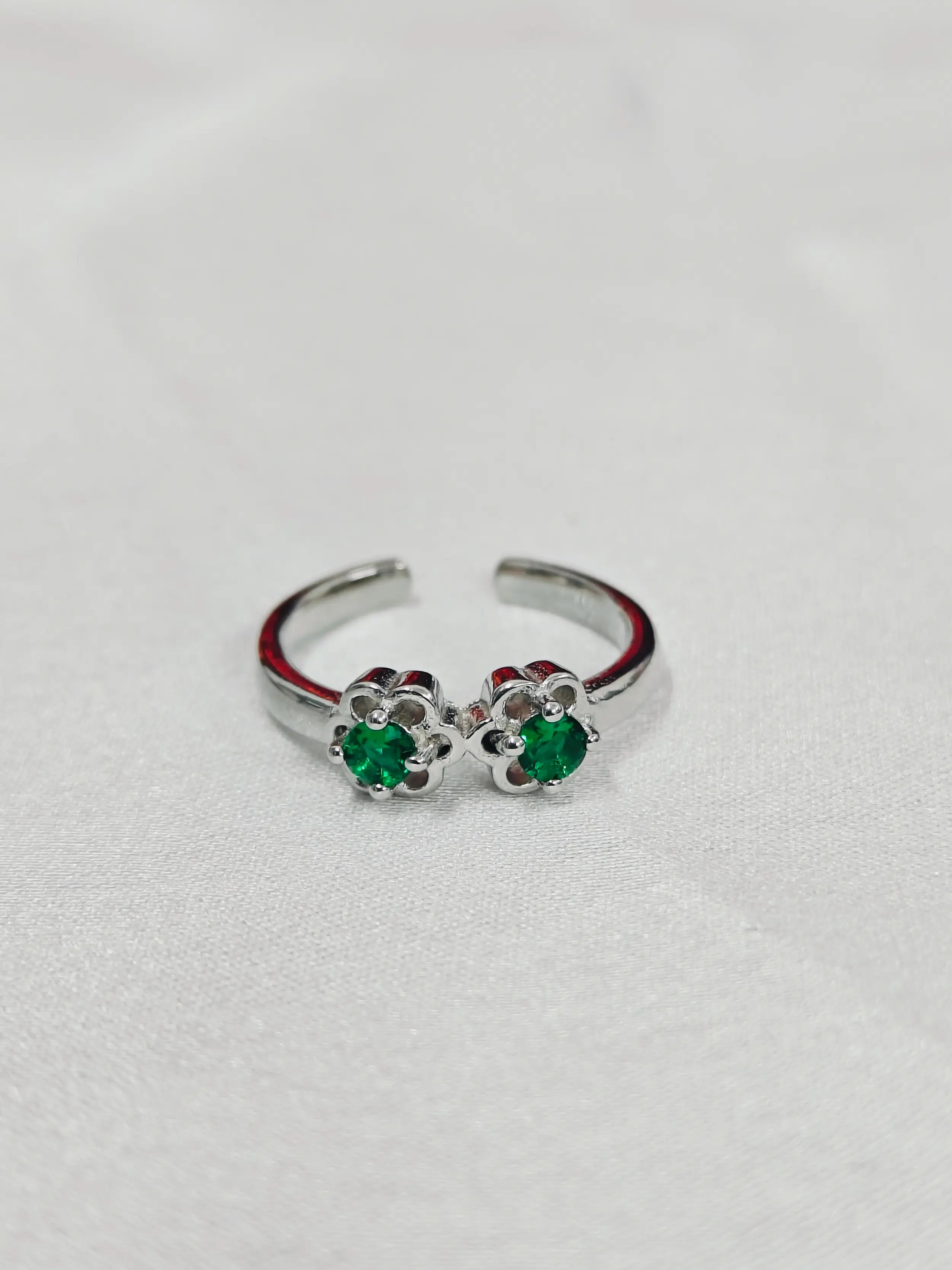 Silver open ring with green gemstones on a light gray background