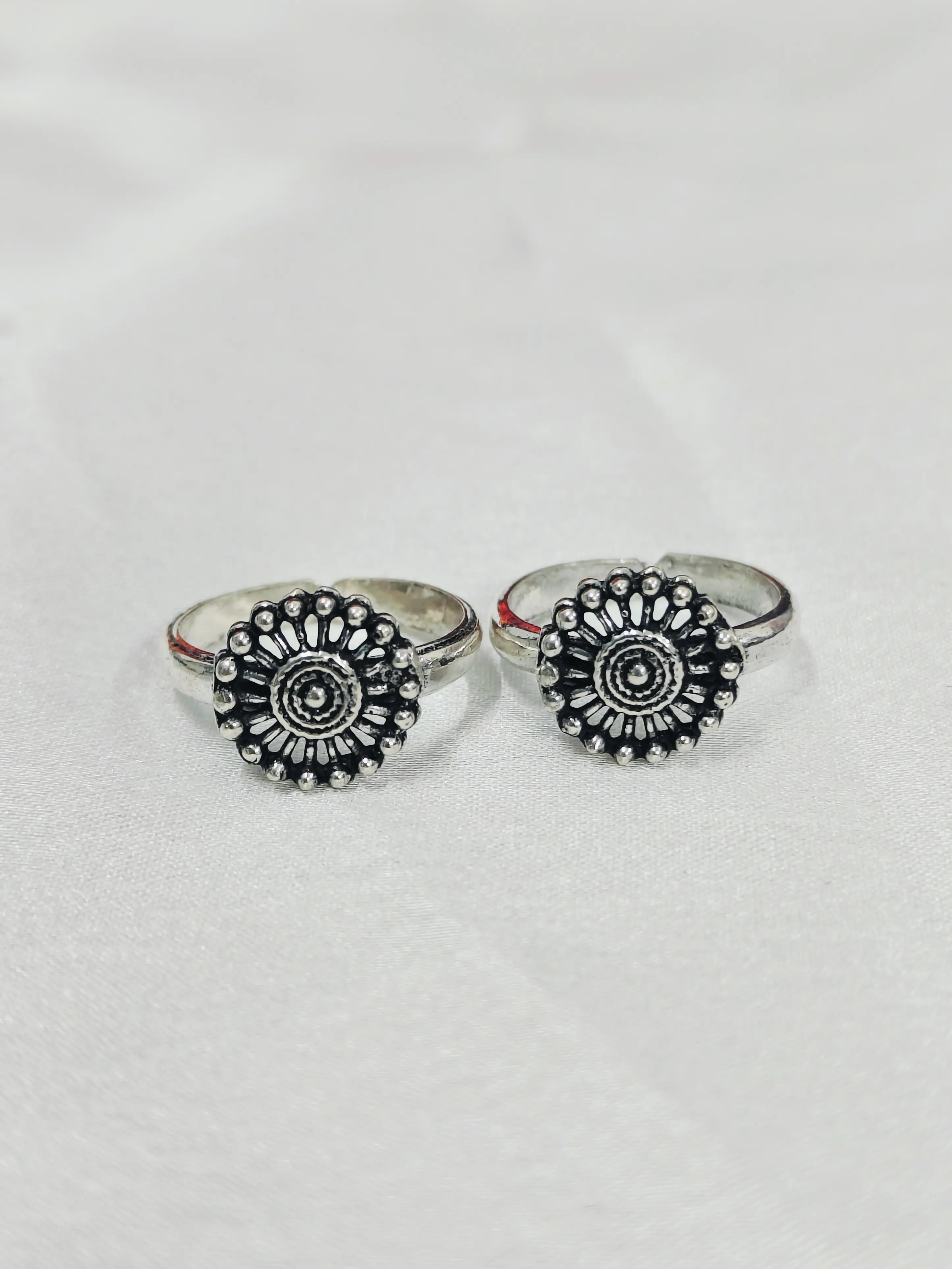 Pair of silver rings with black floral designs on a light gray background