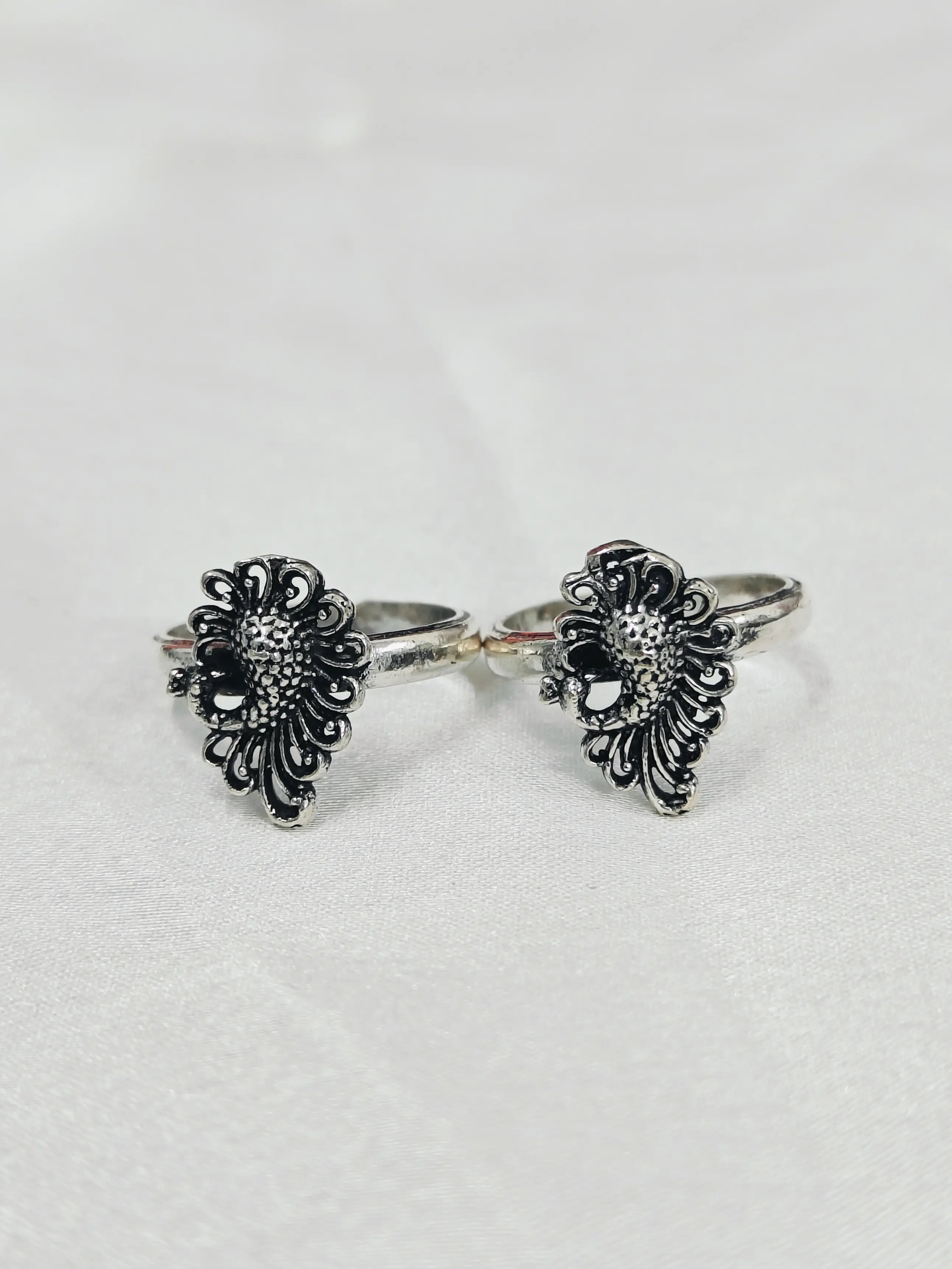 Pair of silver floral cuff bracelets on a light gray background