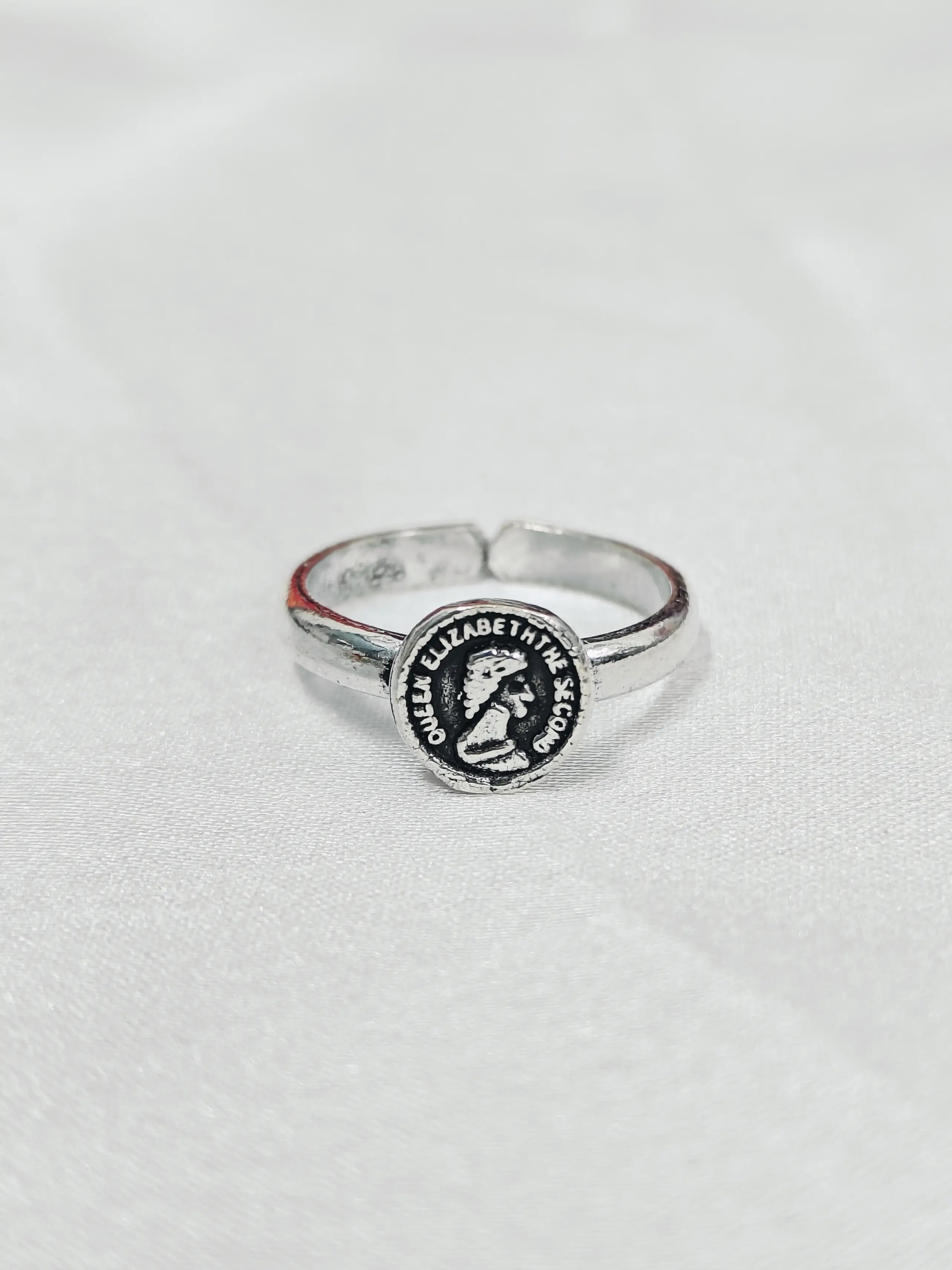 Silver ring with a circular emblem on a light gray background