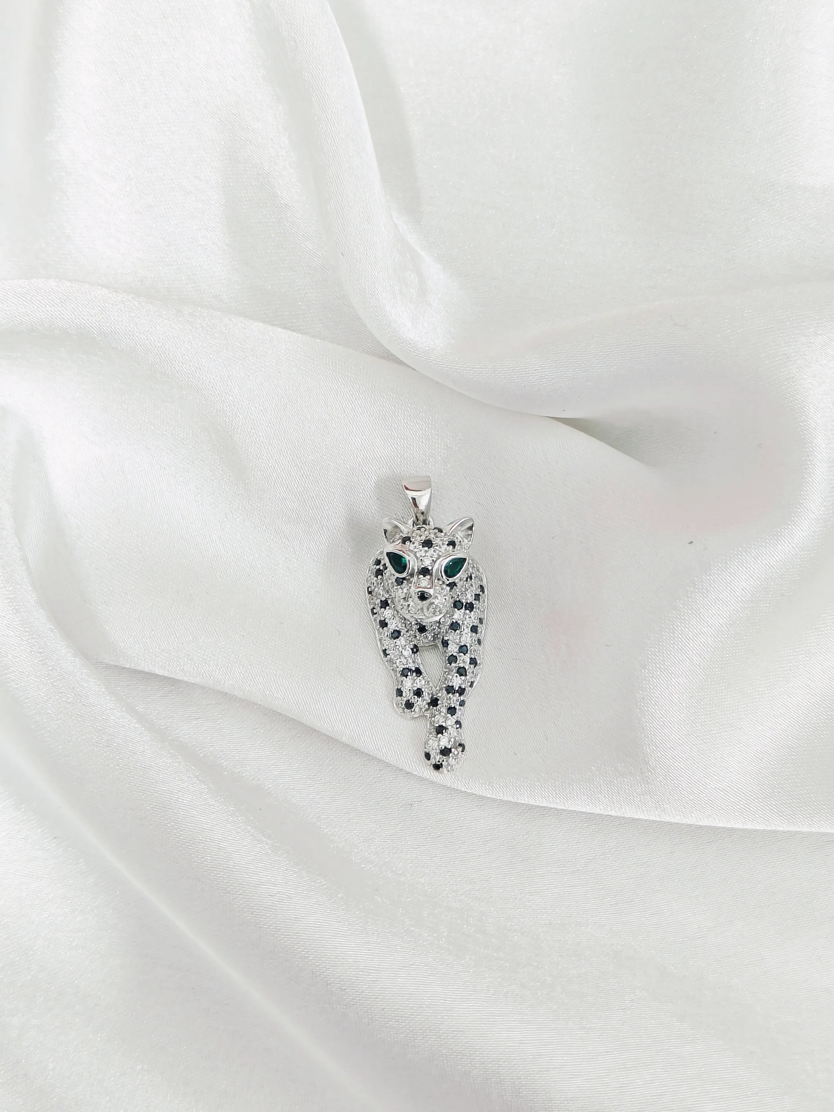 Silver owl-shaped pendant with gemstones on a white satin background