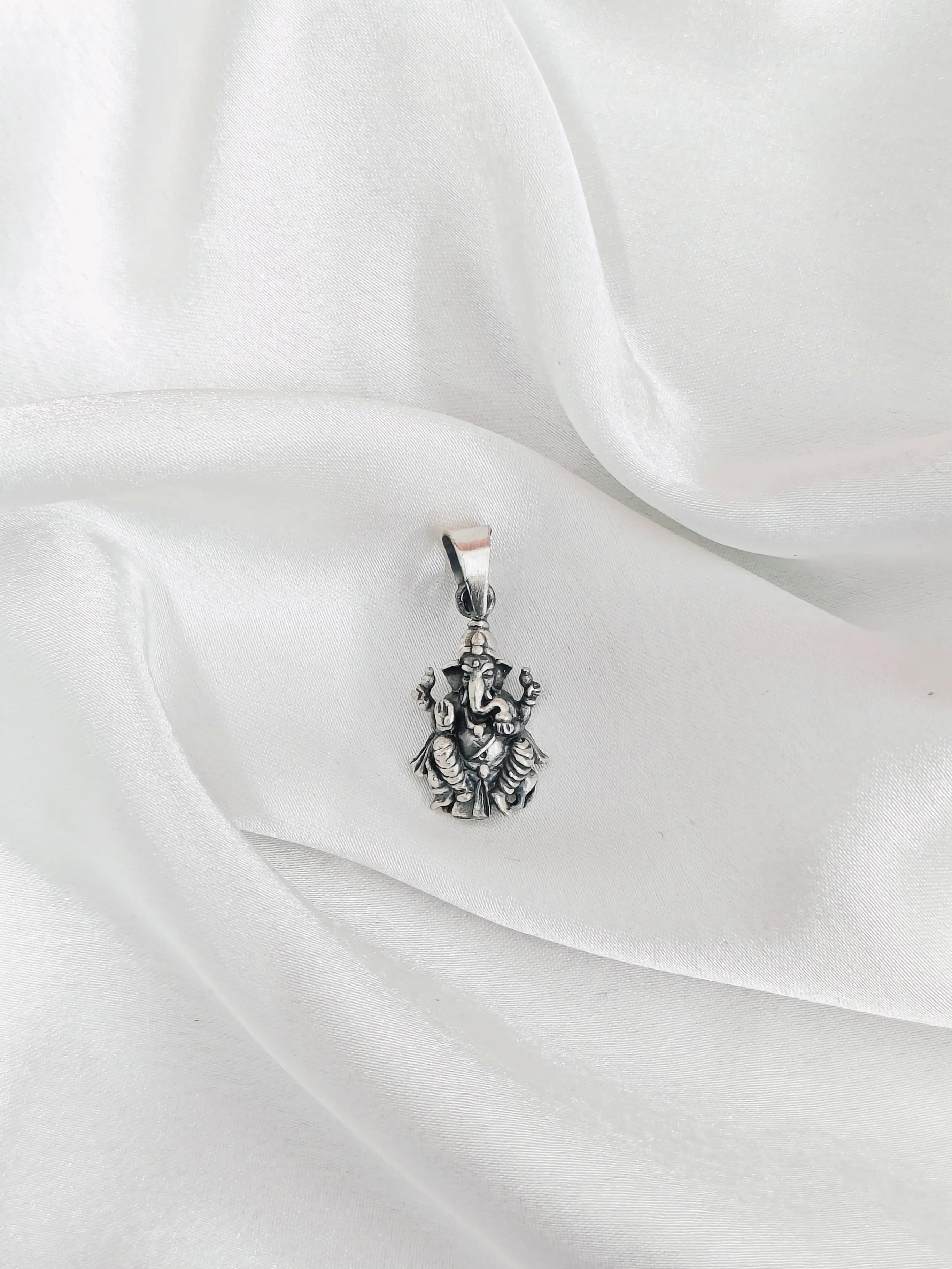 Silver pendant with intricate design on a white fabric background