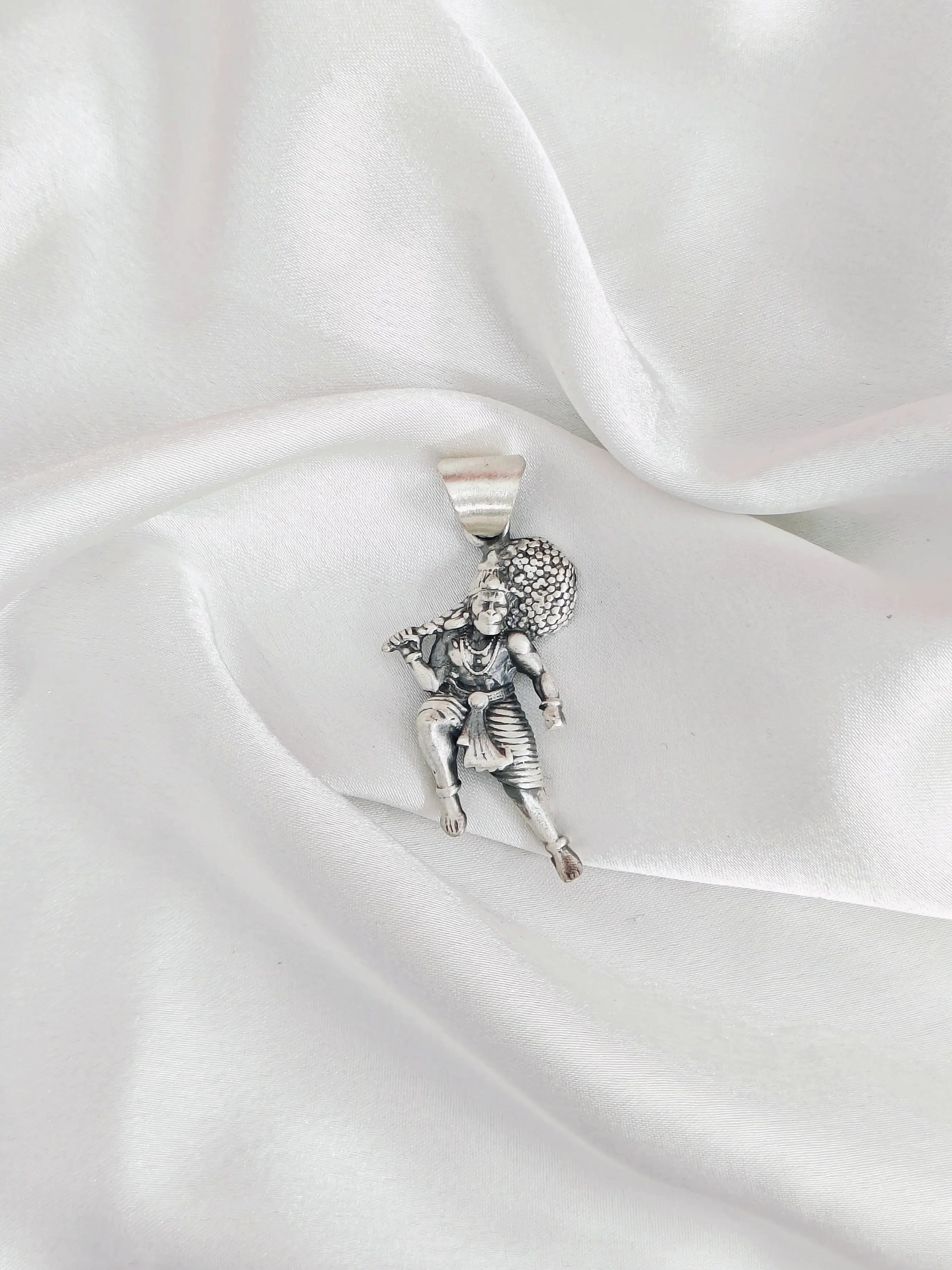 Silver pendant of a figure on a white satin background