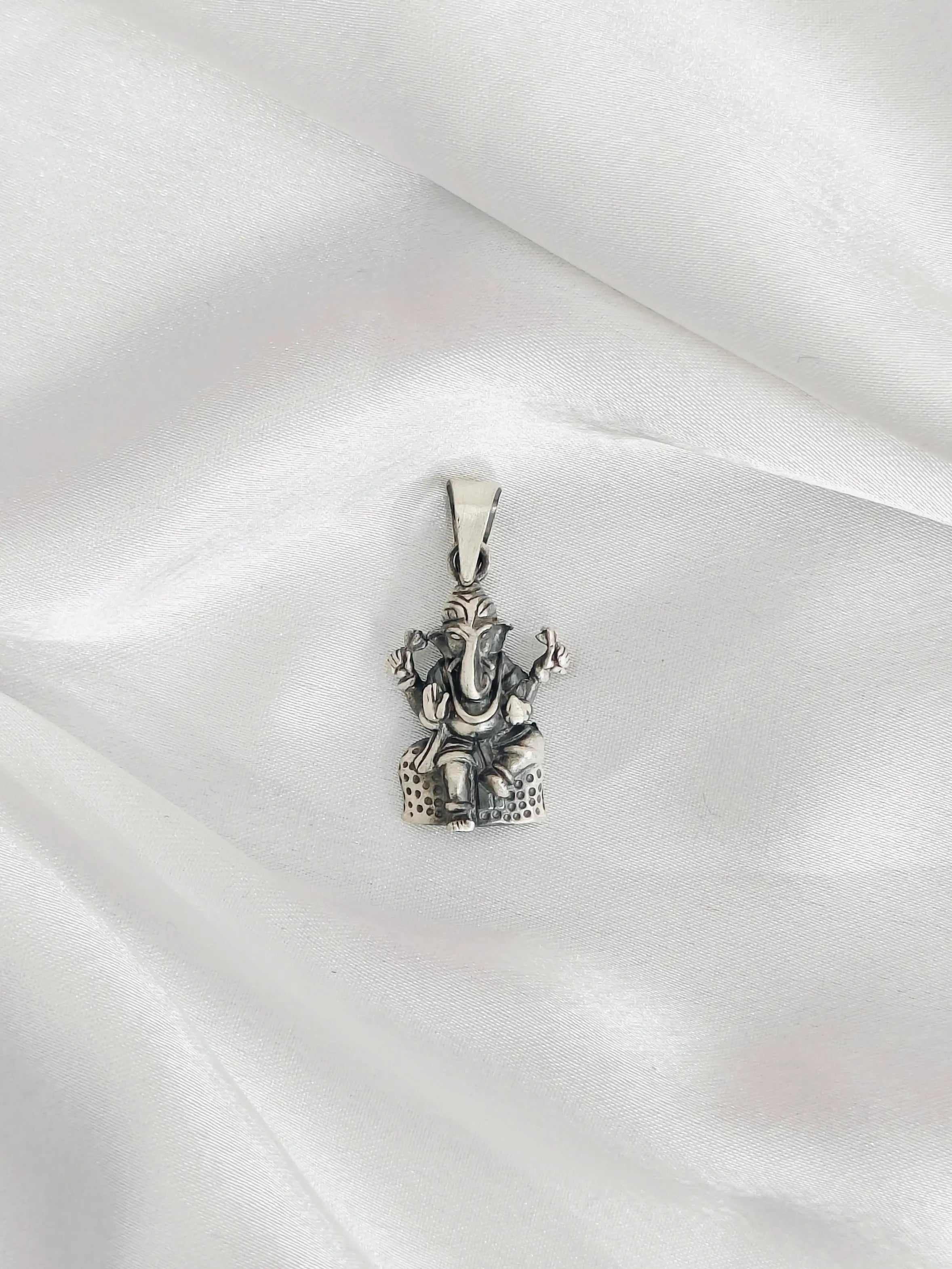 Silver pendant of a deity figure on a white fabric background