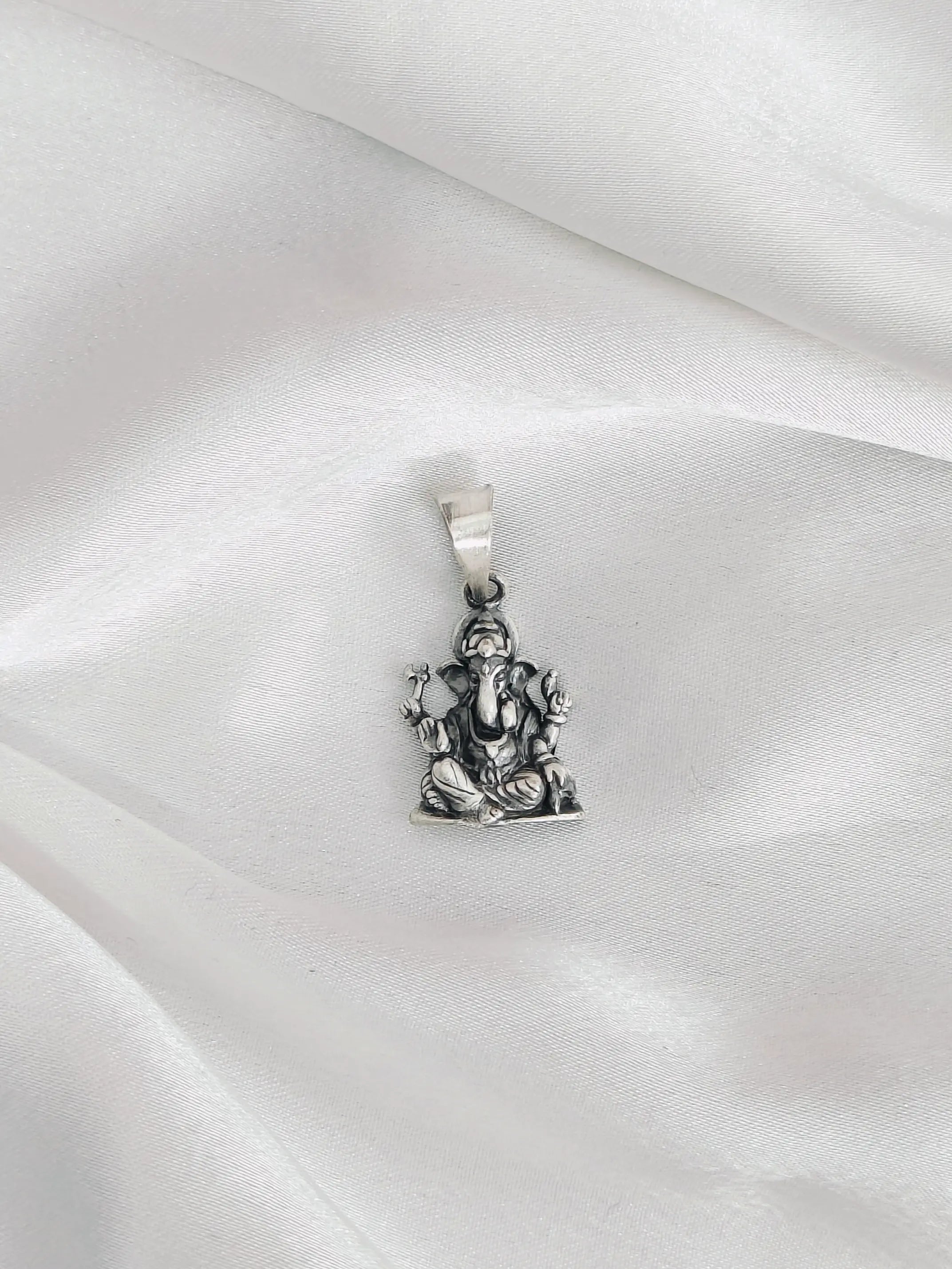 Silver pendant of a deity figure on a white satin background