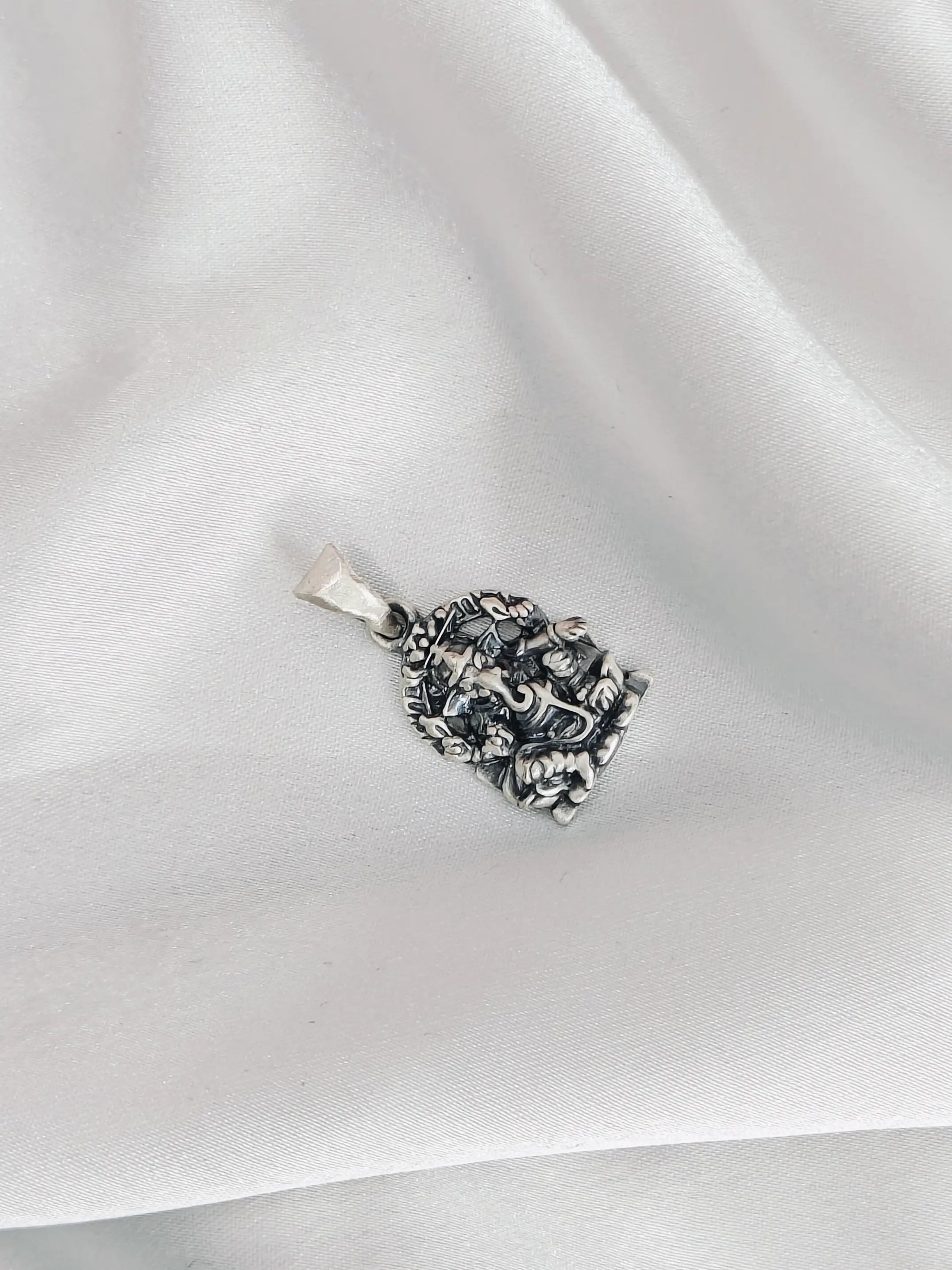 Silver pendant with intricate design on a white fabric background