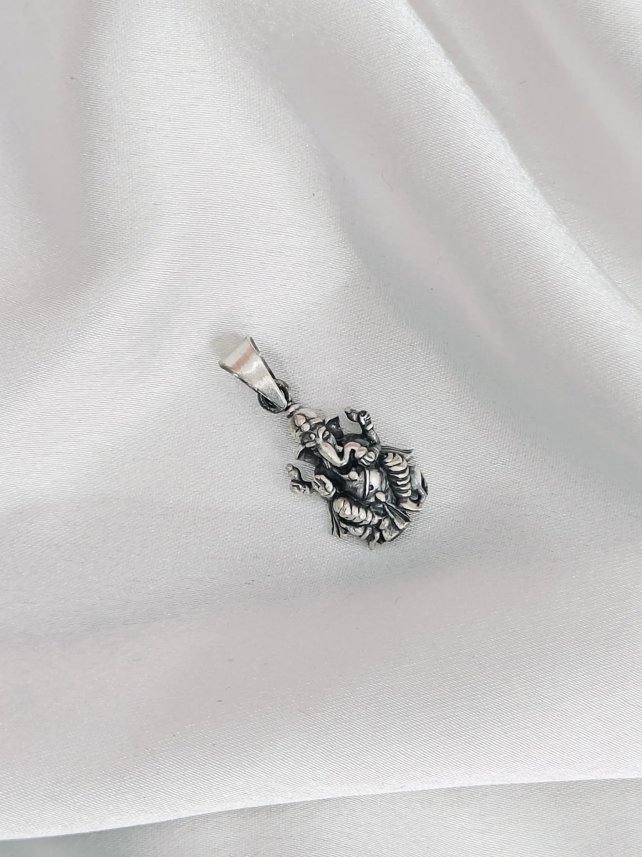 Silver pendant with intricate design on a white fabric background